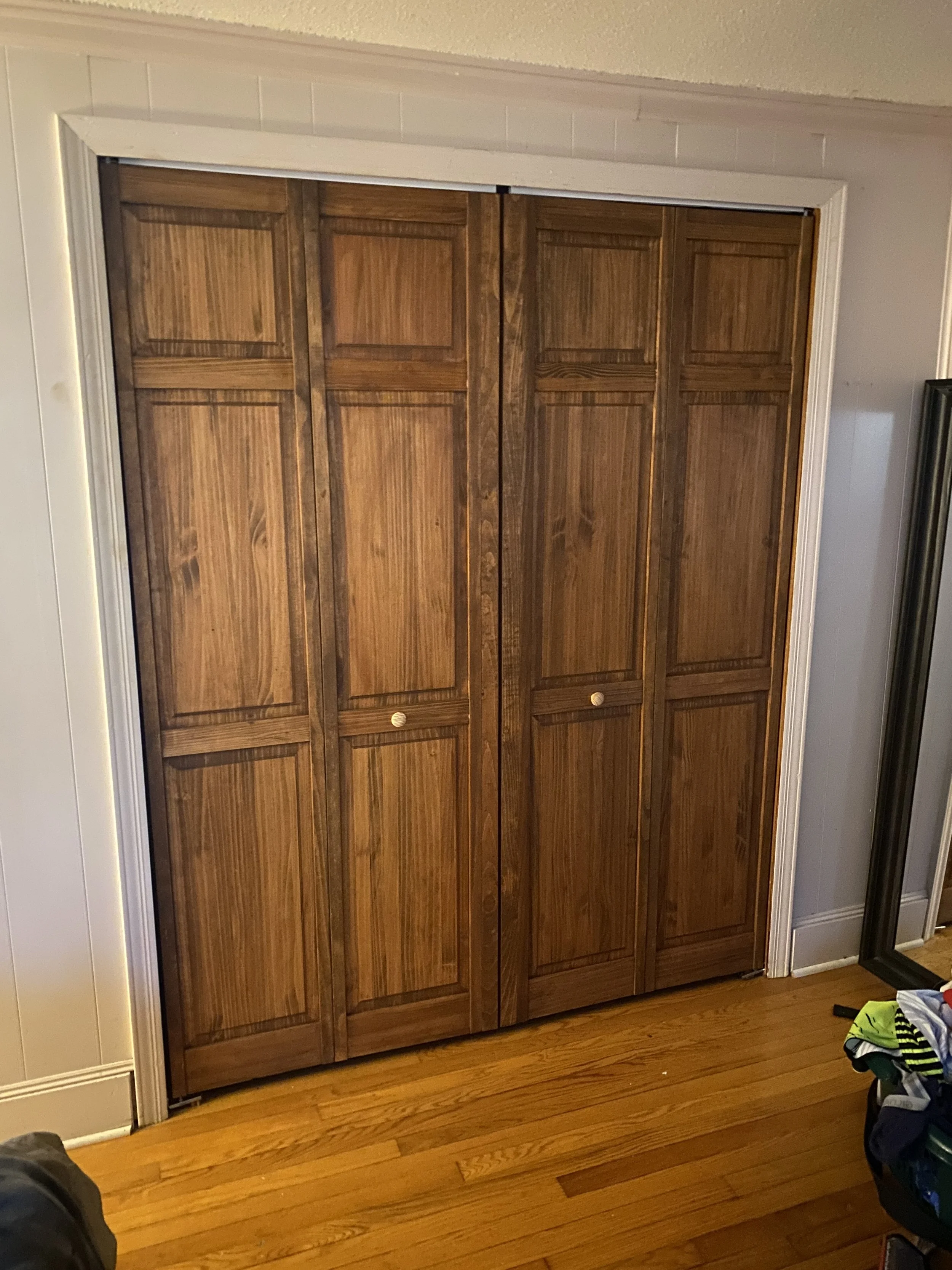 Wooden sliding closet doors inside a room with hardwood flooring and white trim.