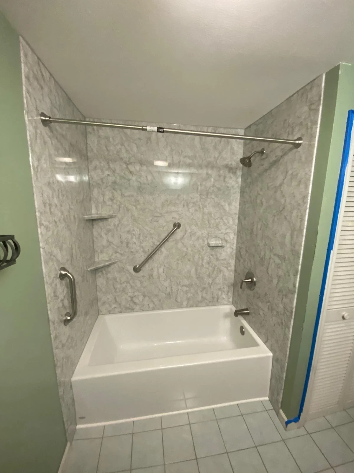 Accessible shower with marble tiles, a bathtub, metal grab bars, and a sliding shower curtain rod.