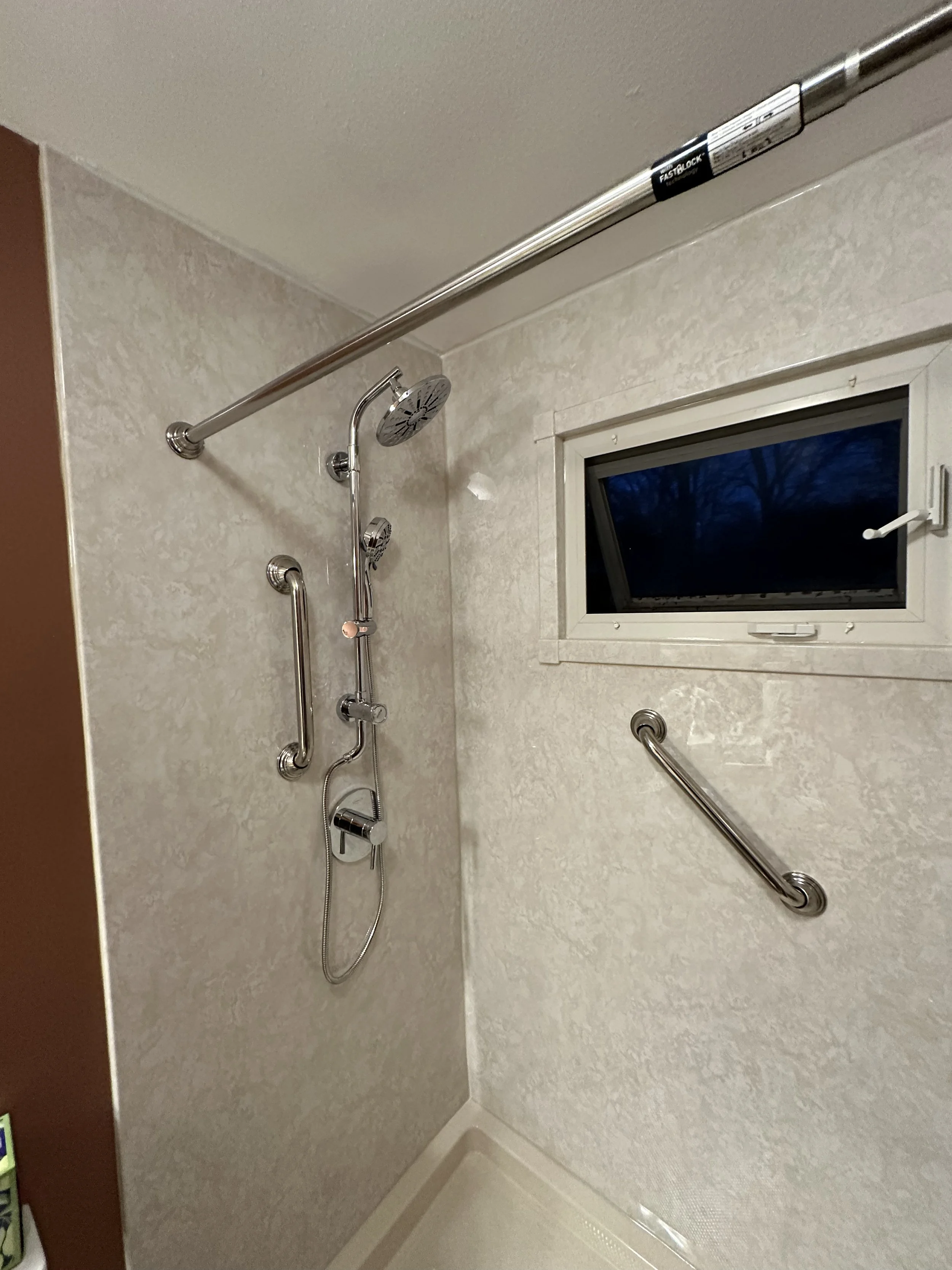A shower area with multiple silver showerheads, grab bars, and a small window showing a dark sky outside.