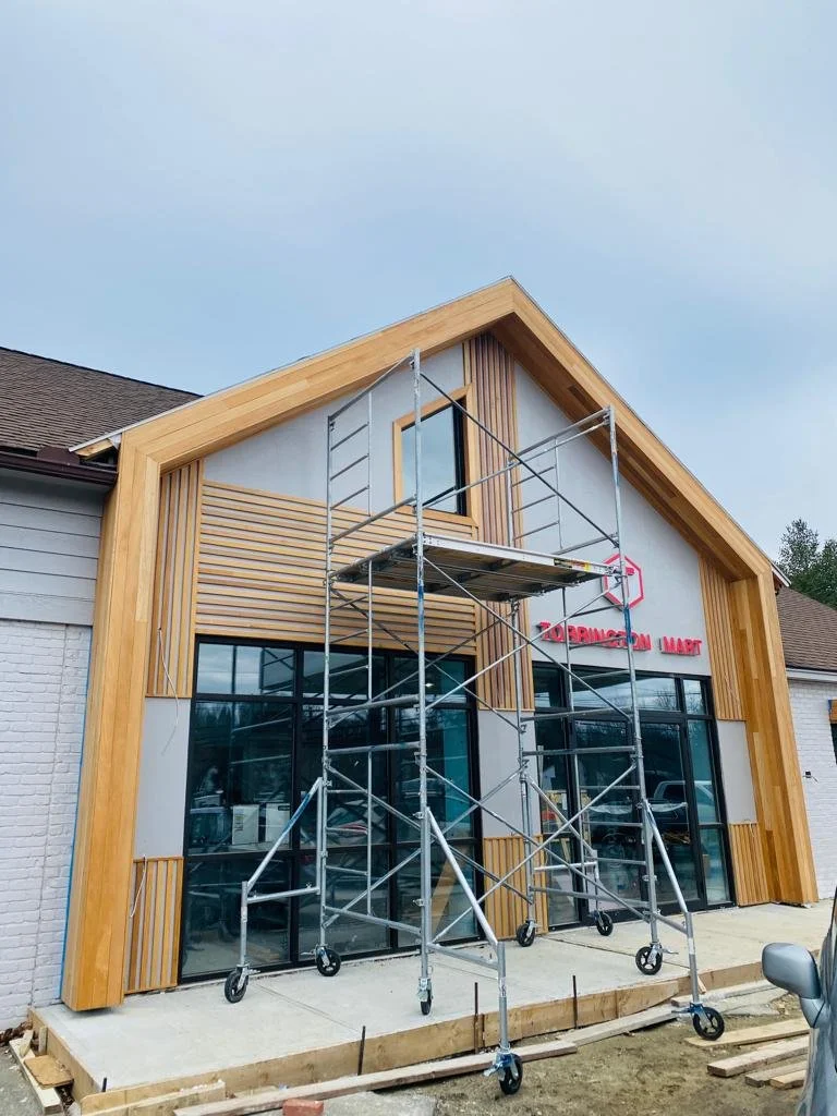 Construction scaffolding set up outside a new building with large glass doors, wooden accents, and a sign reading 'Zobiacon Mart'.