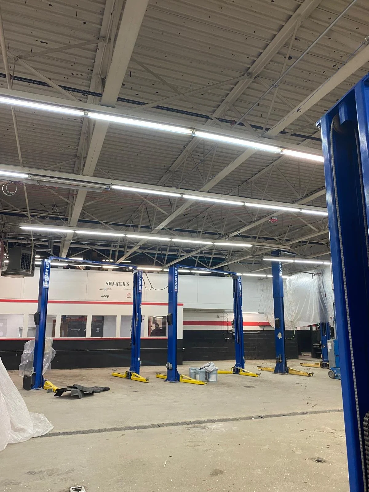 Inside an automotive repair shop with four blue car lifts, some tools, and a partial view of a black and white building.