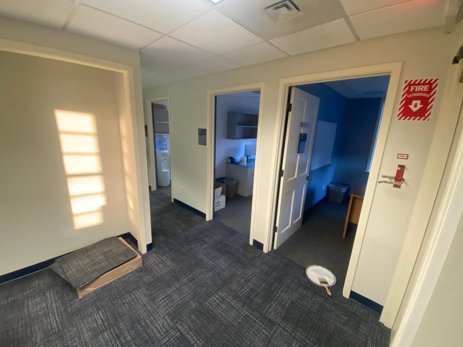 Office hallway with three open doors, a water cooler, and a fire safety sign on the wall.