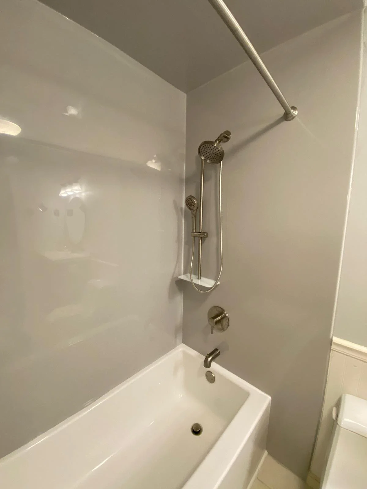 Bathroom with a bathtub, two showerheads, a wall mounted soap shelf, and a toilet.