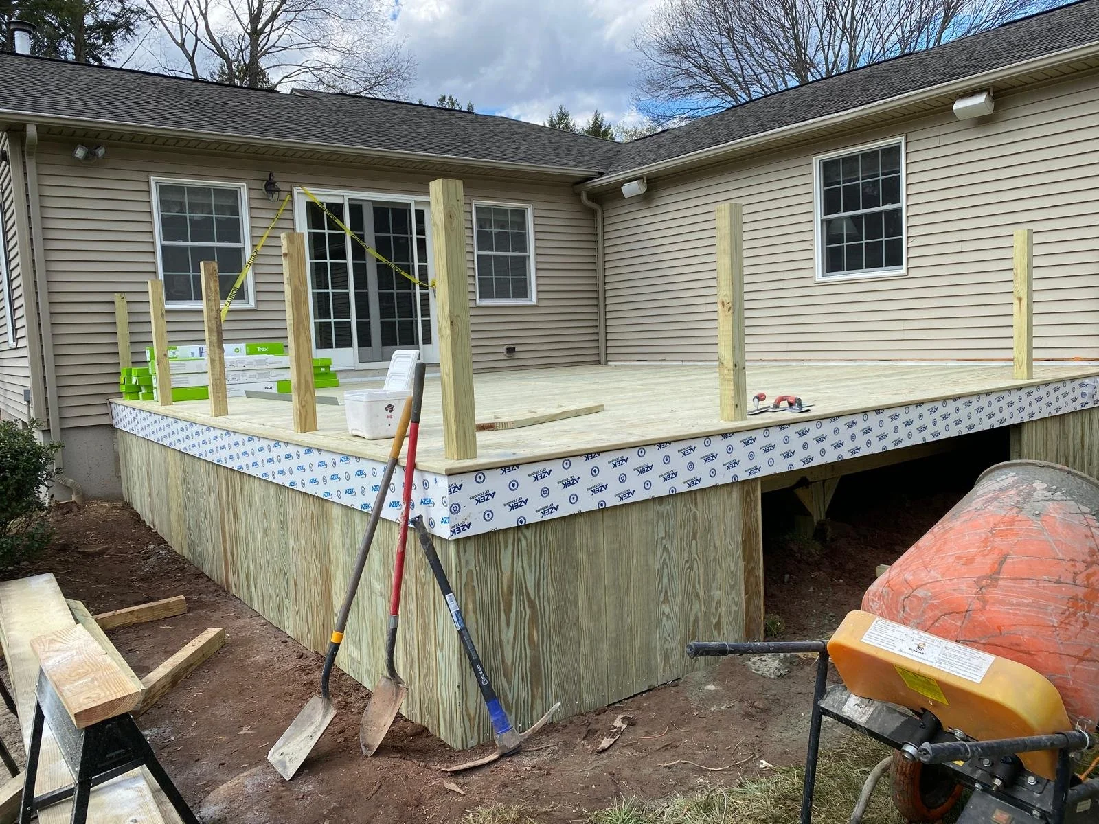 Under construction wooden deck attached to a house with siding, with tools and materials present.