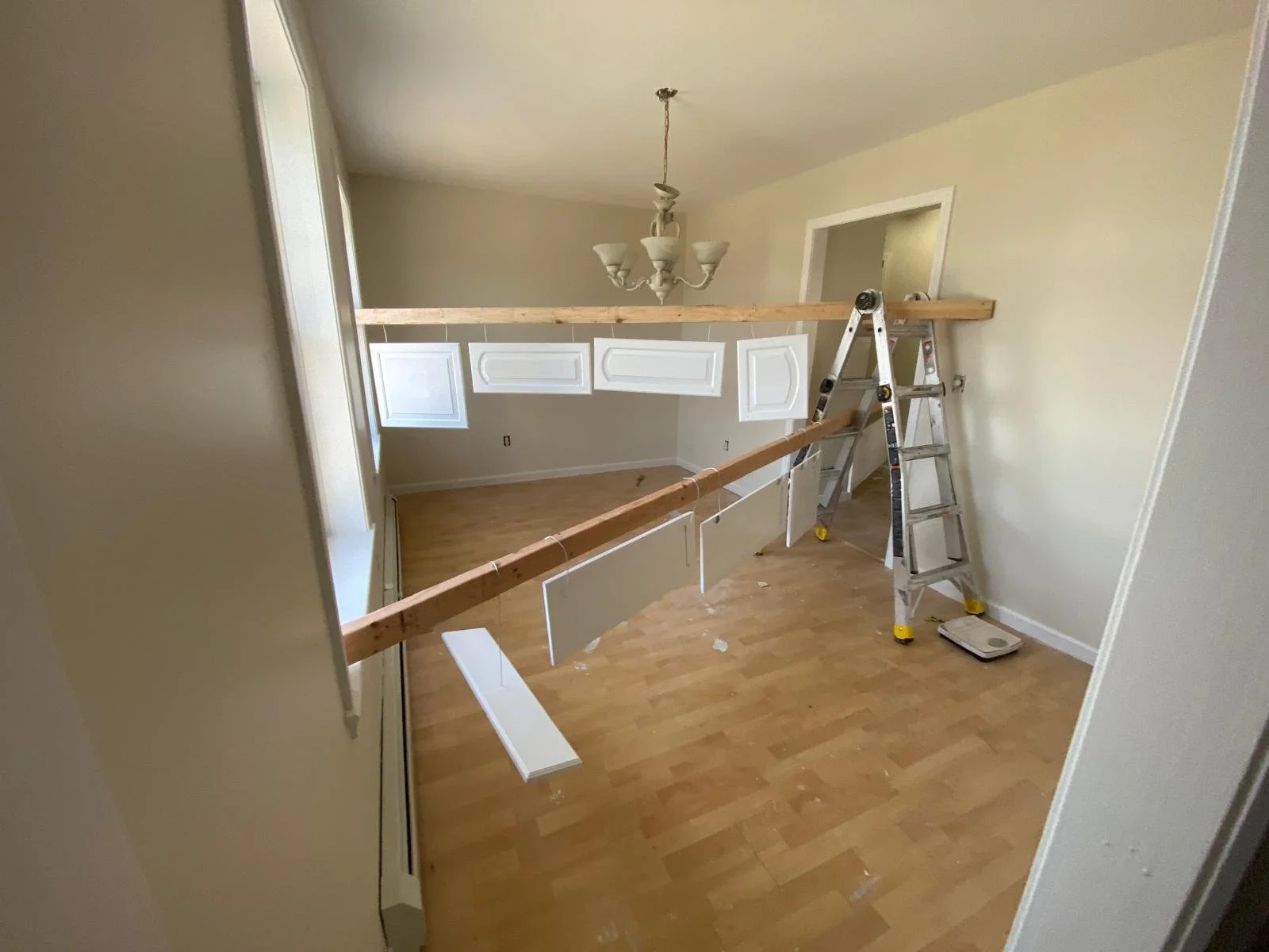 A room under renovation with a ladder, wooden beams, and white wall panels being installed or repaired.