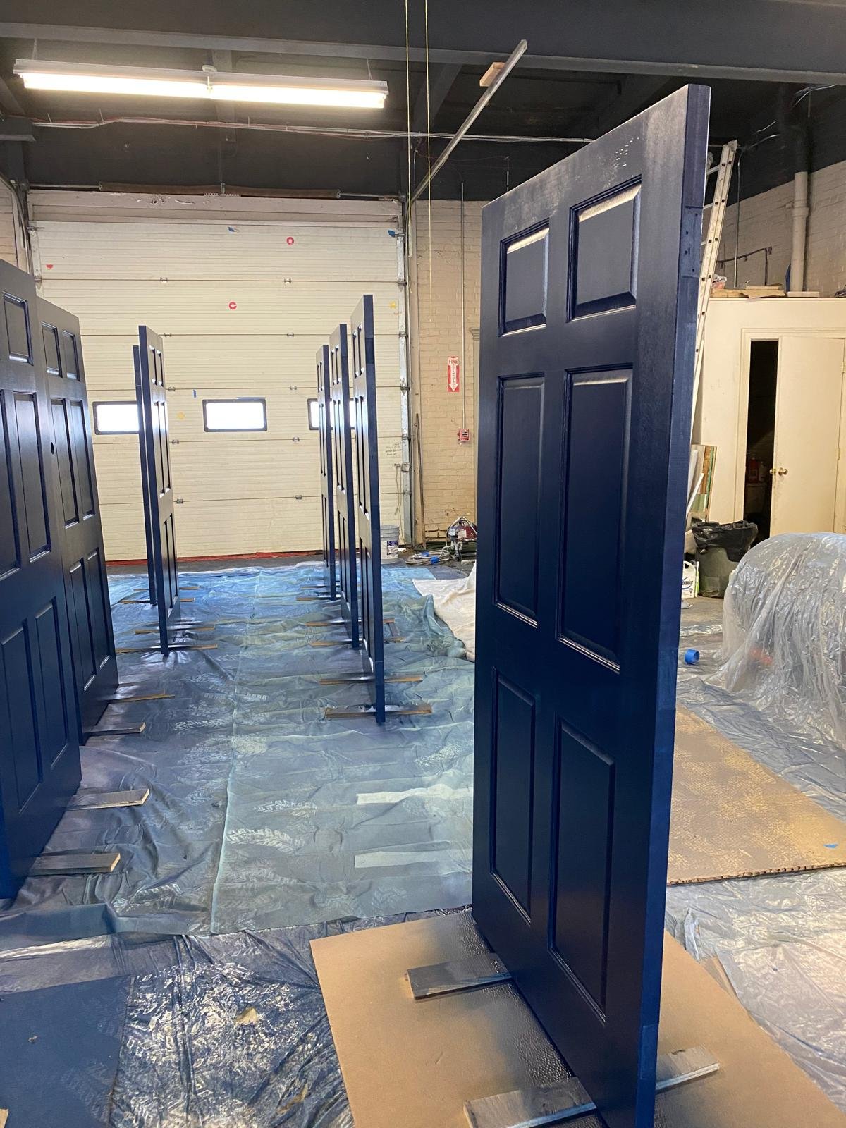 Interior of a workshop or garage with several painted blue doors standing on protective sheets, ready for installation.