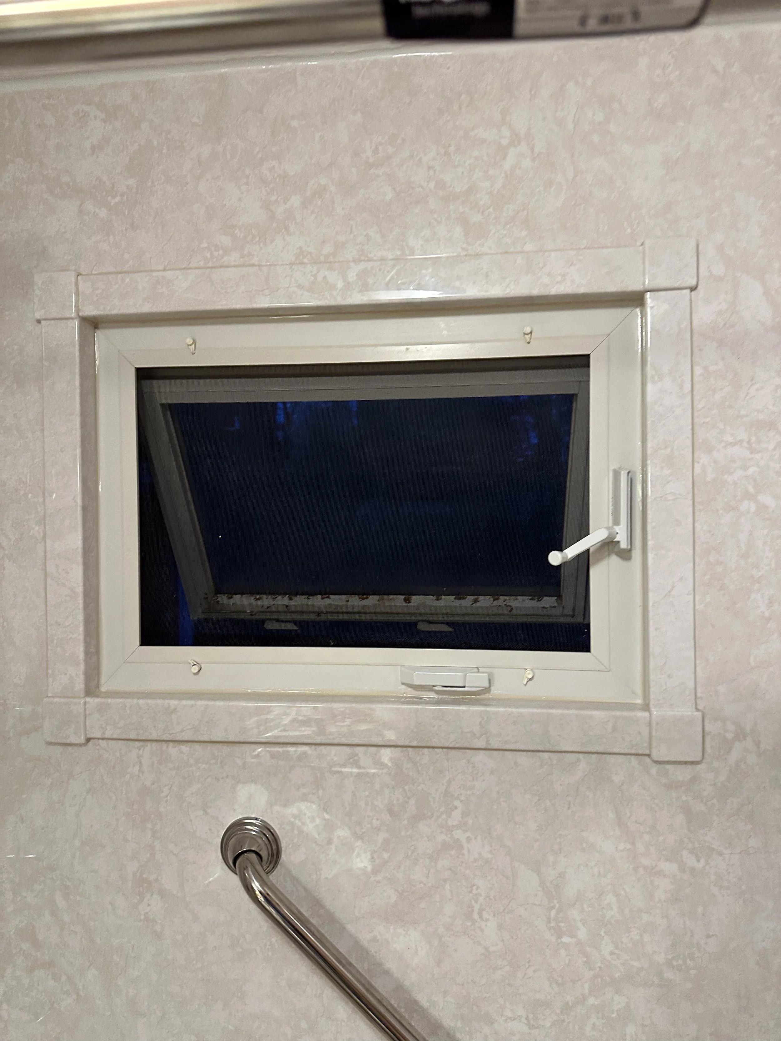 A small rectangular window with a white frame and a handle, set in a beige wall. An exterior darkness is visible through the window.