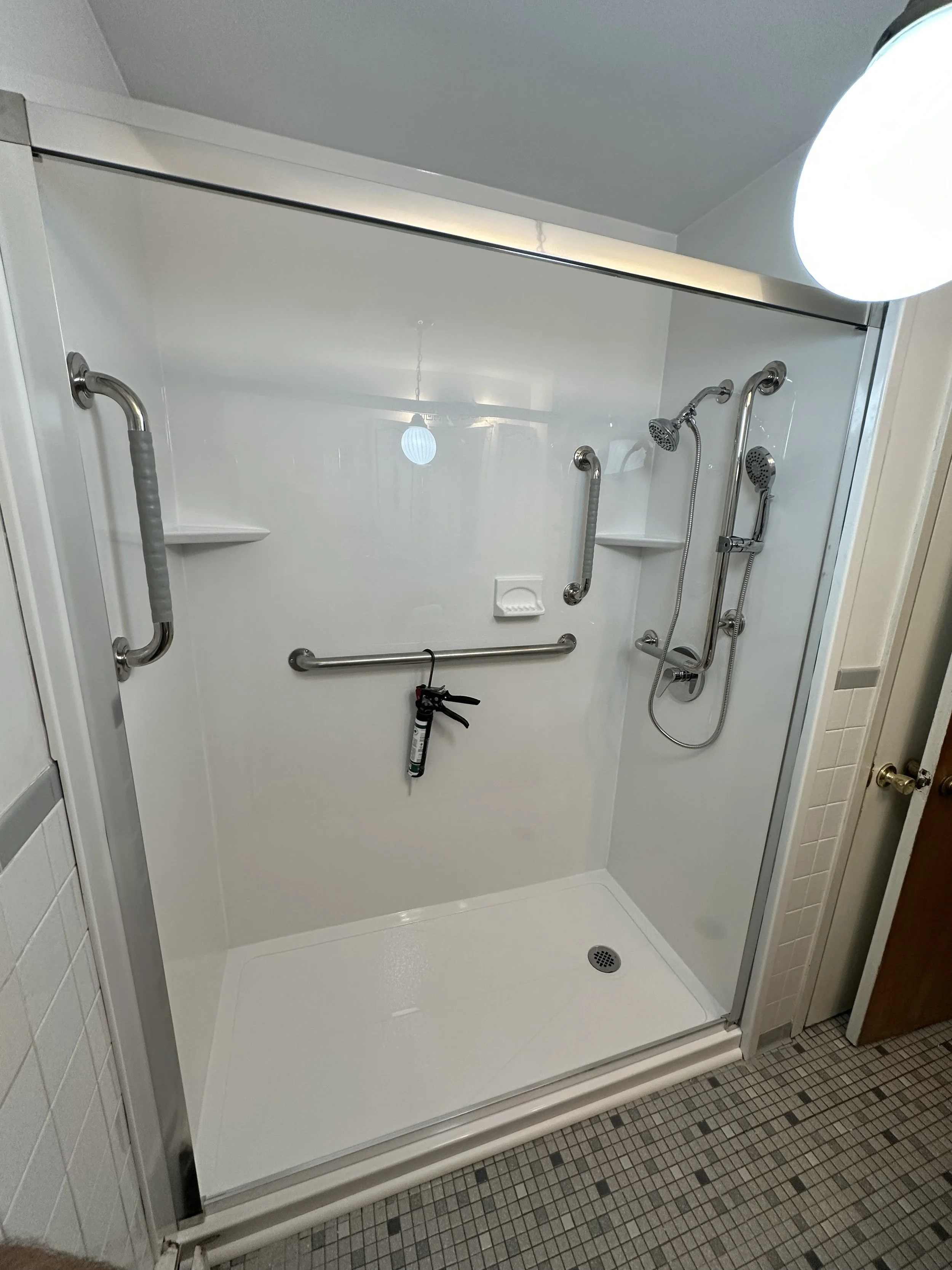 Empty walk-in shower with white walls, multiple showerheads, safety grab bars, soap dish, and a set of keys hanging from one of the bars.