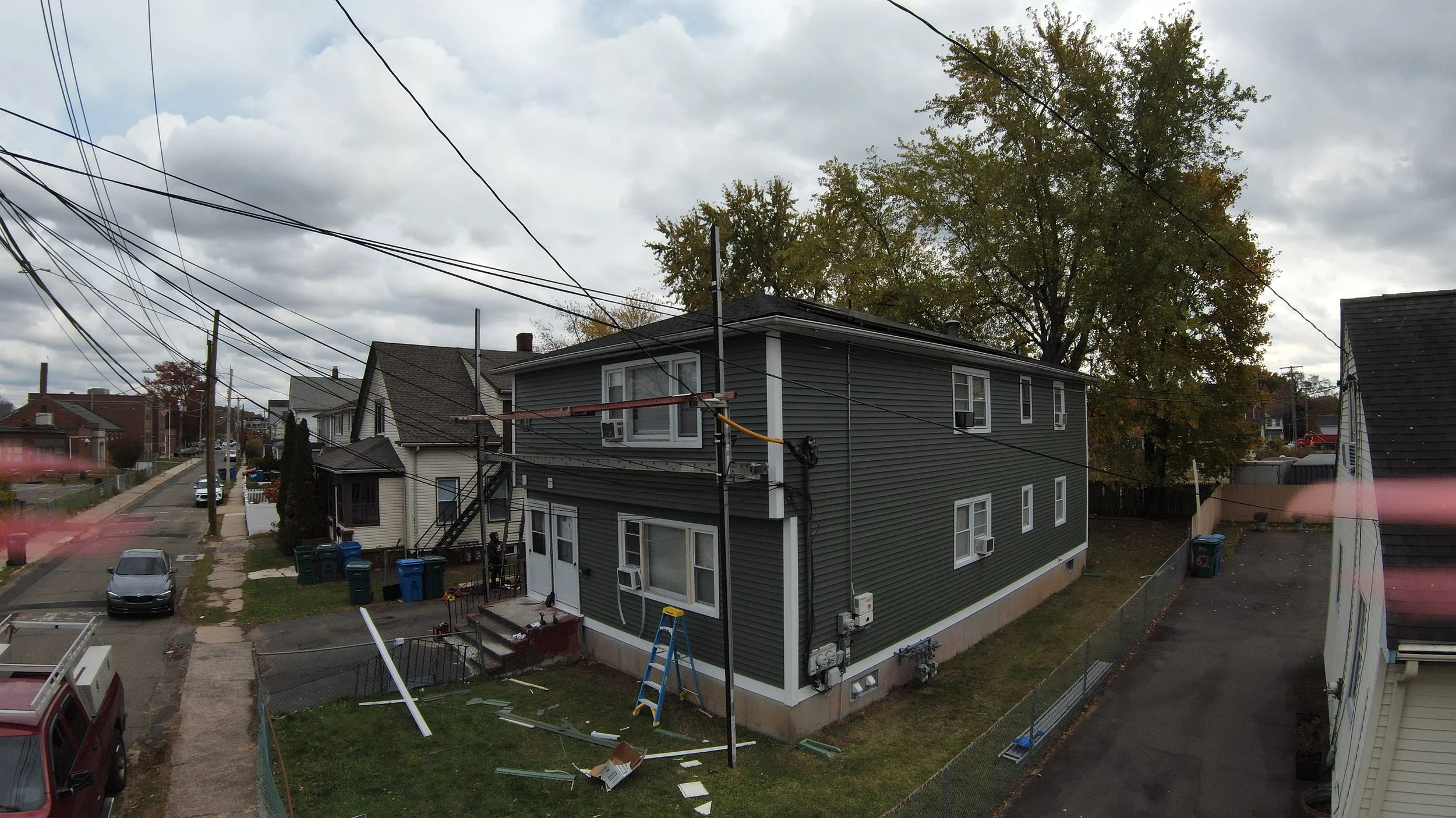 Backyard of a gray house with storm damage, fallen roof pieces, and debris scattered on the lawn, under cloudy sky.