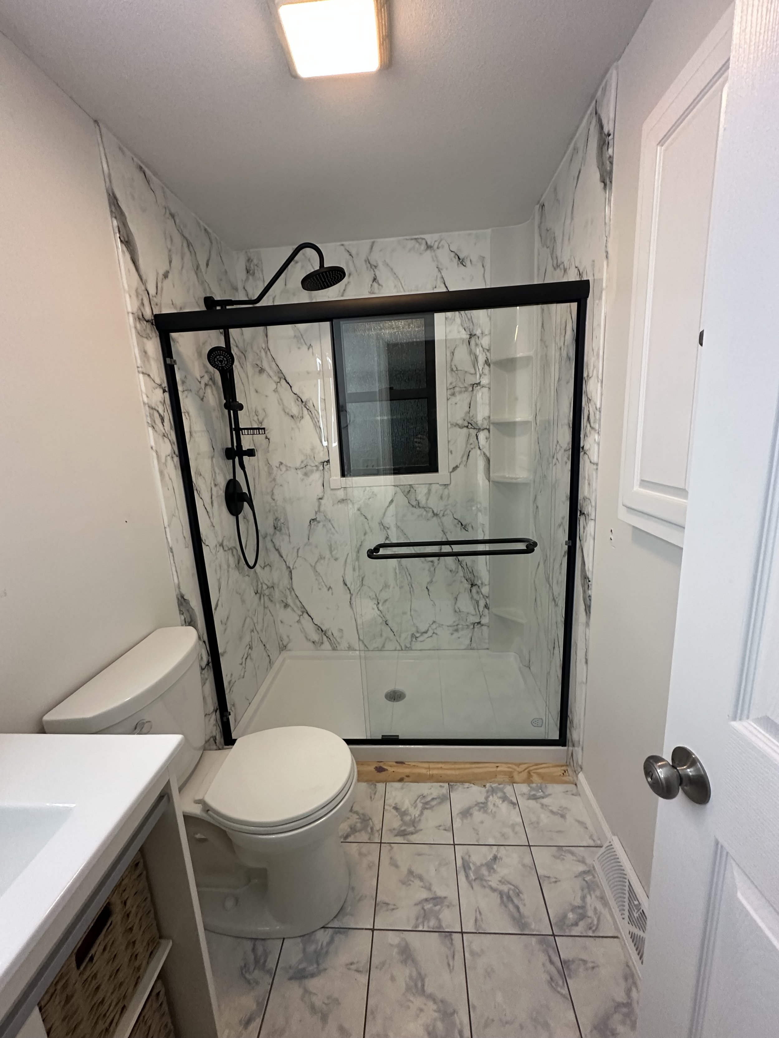 Bathroom with a toilet, a white vanity, and a walk-in shower with black framing and marble walls.