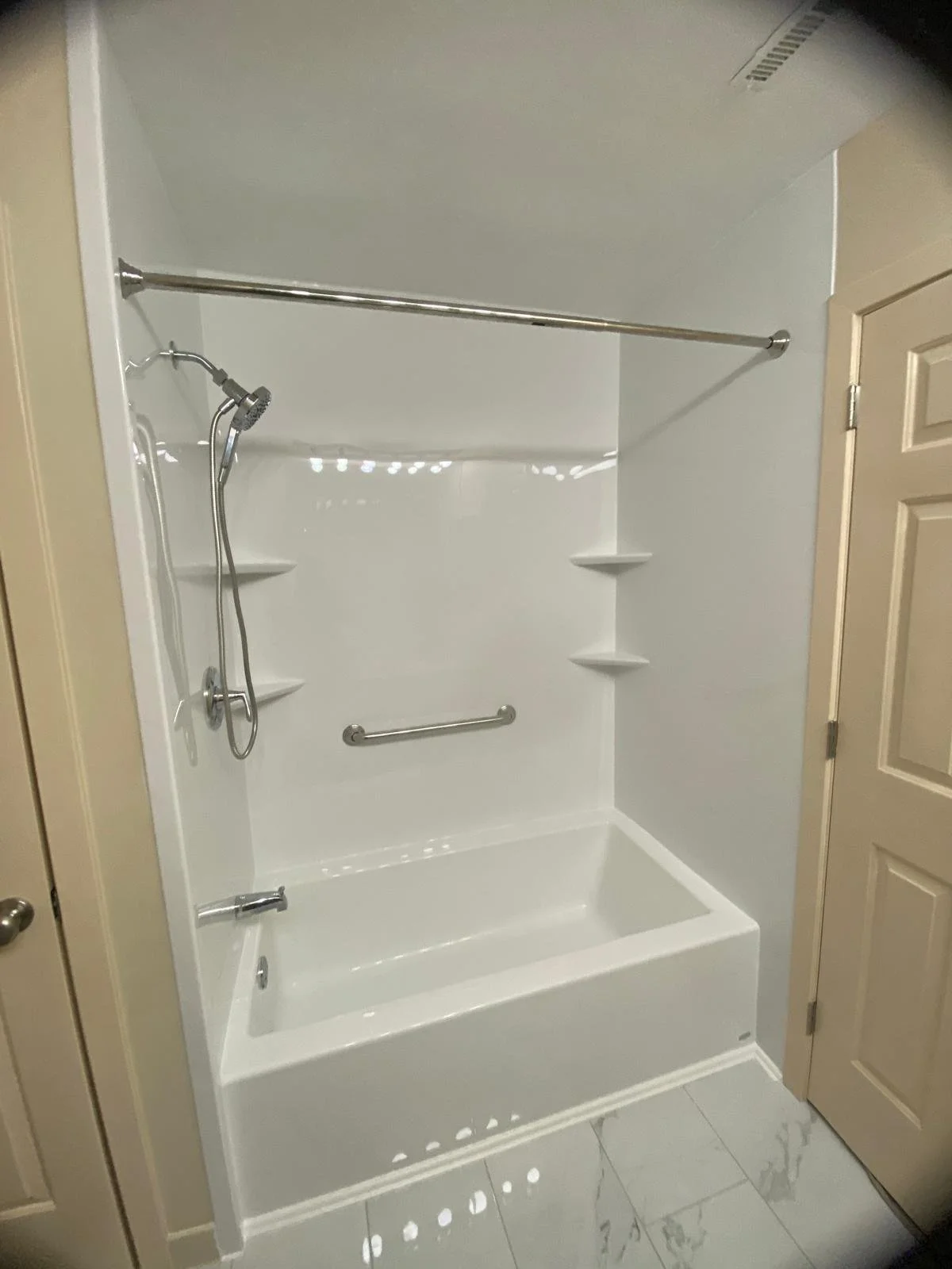 Empty white bathtub with a showerhead and silver grab bars inside a bathroom corner.