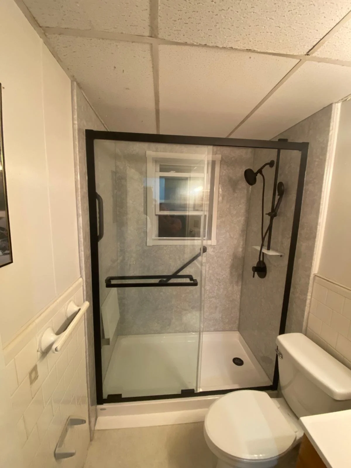 A small bathroom with a bathtub and shower combination, a toilet, a window, and white tiled walls.