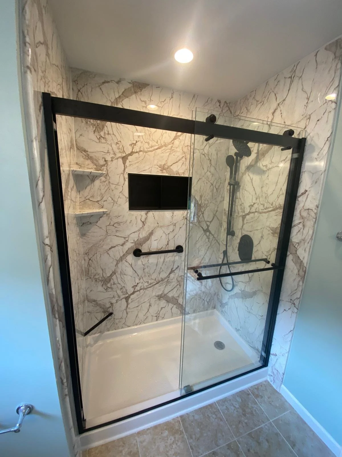 A glass-enclosed shower with marble walls, black fixtures, and a built-in niche with shelves.
