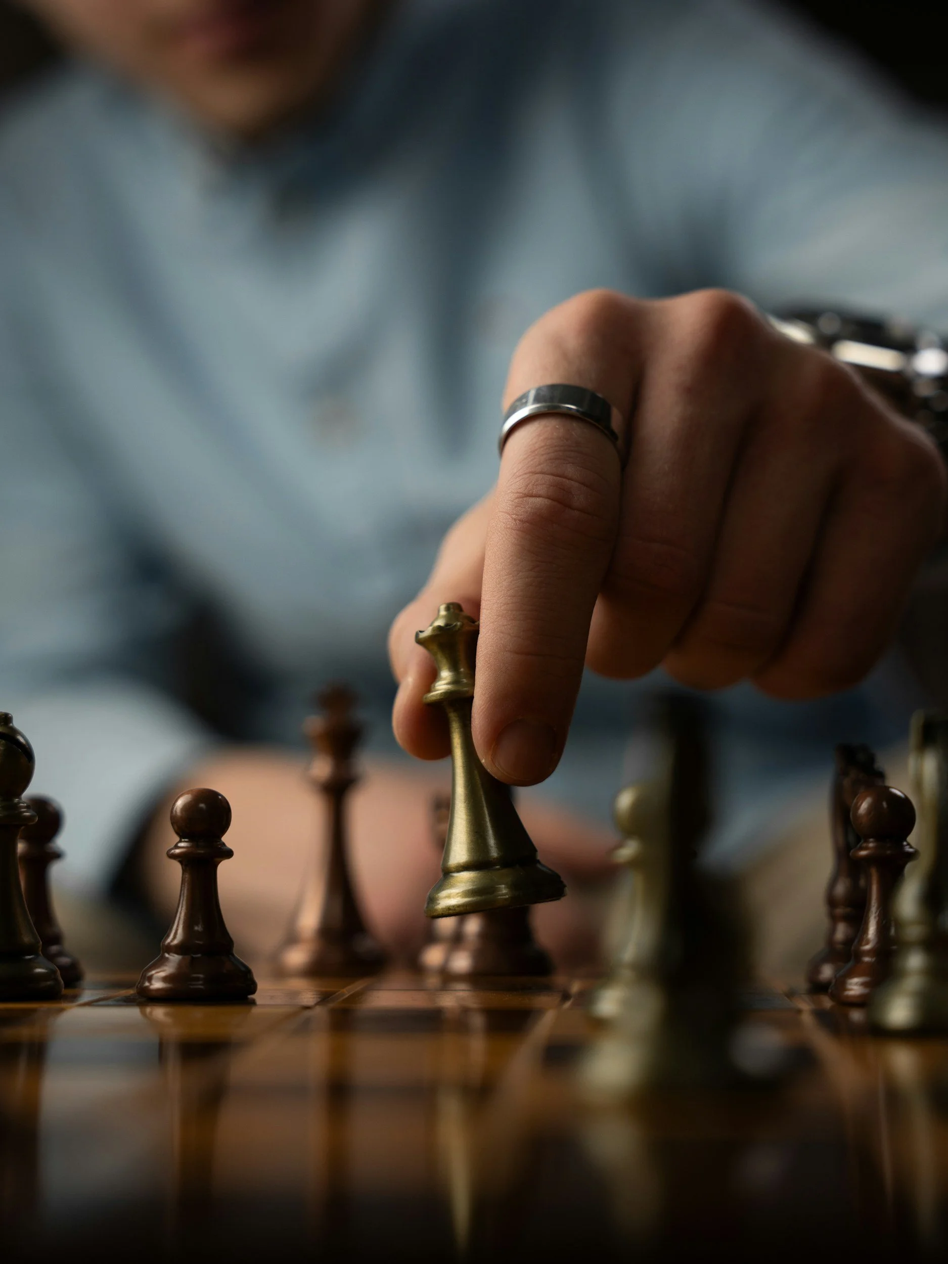 A close-up of a hand moving a gold king chess piece on a wooden chessboard, with other chess pieces visible in the background.
