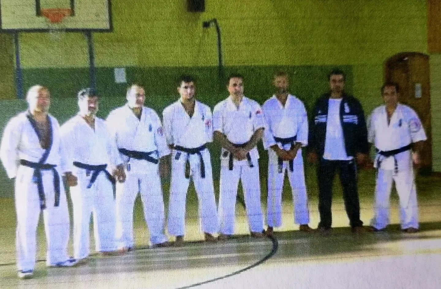 Gruppe von Kampfsportlern in Gi-Uniformen, die in einer Turnhalle stehen.