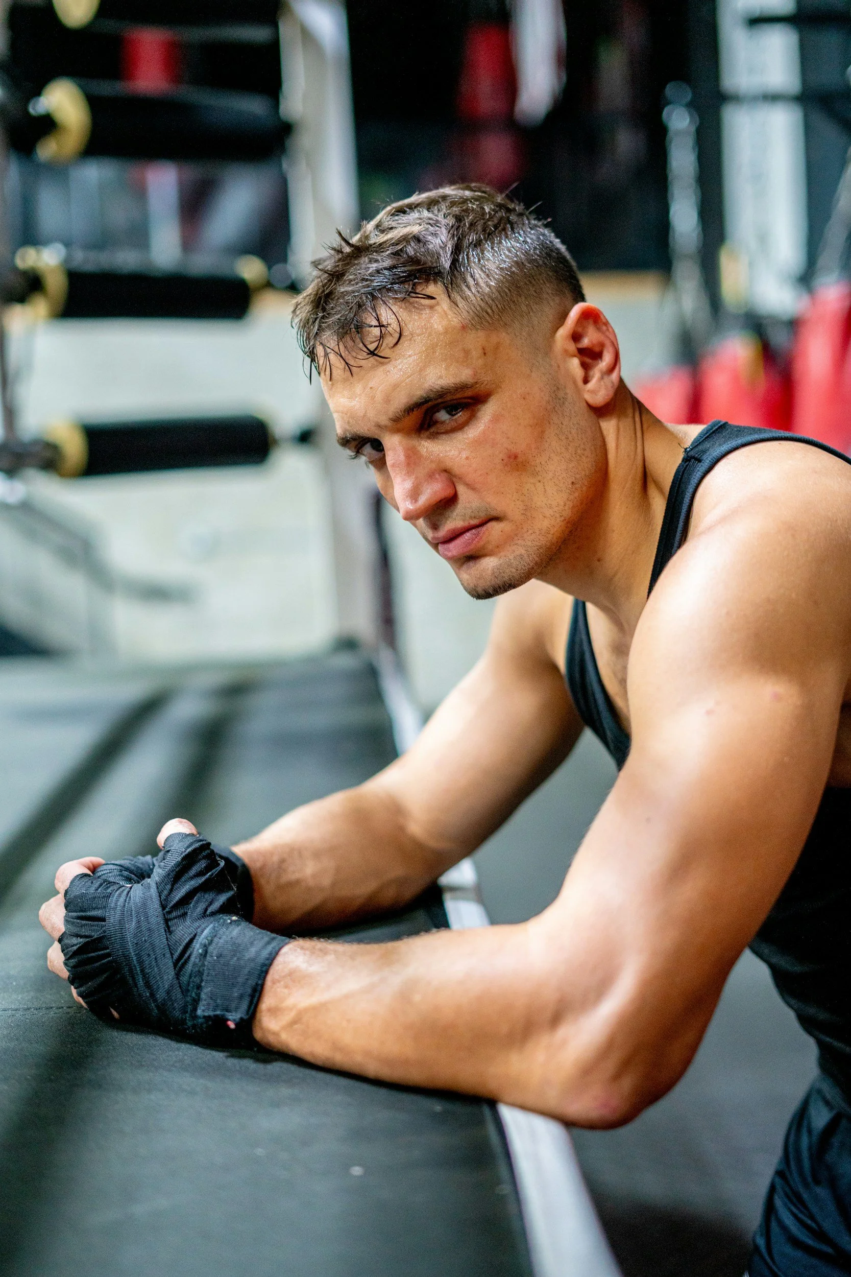 Ein junger Mann beim Boxtraining in einem Fitnessstudio, lehnte an einem schwarzen Trainingssitz und schaut in die Kamera.