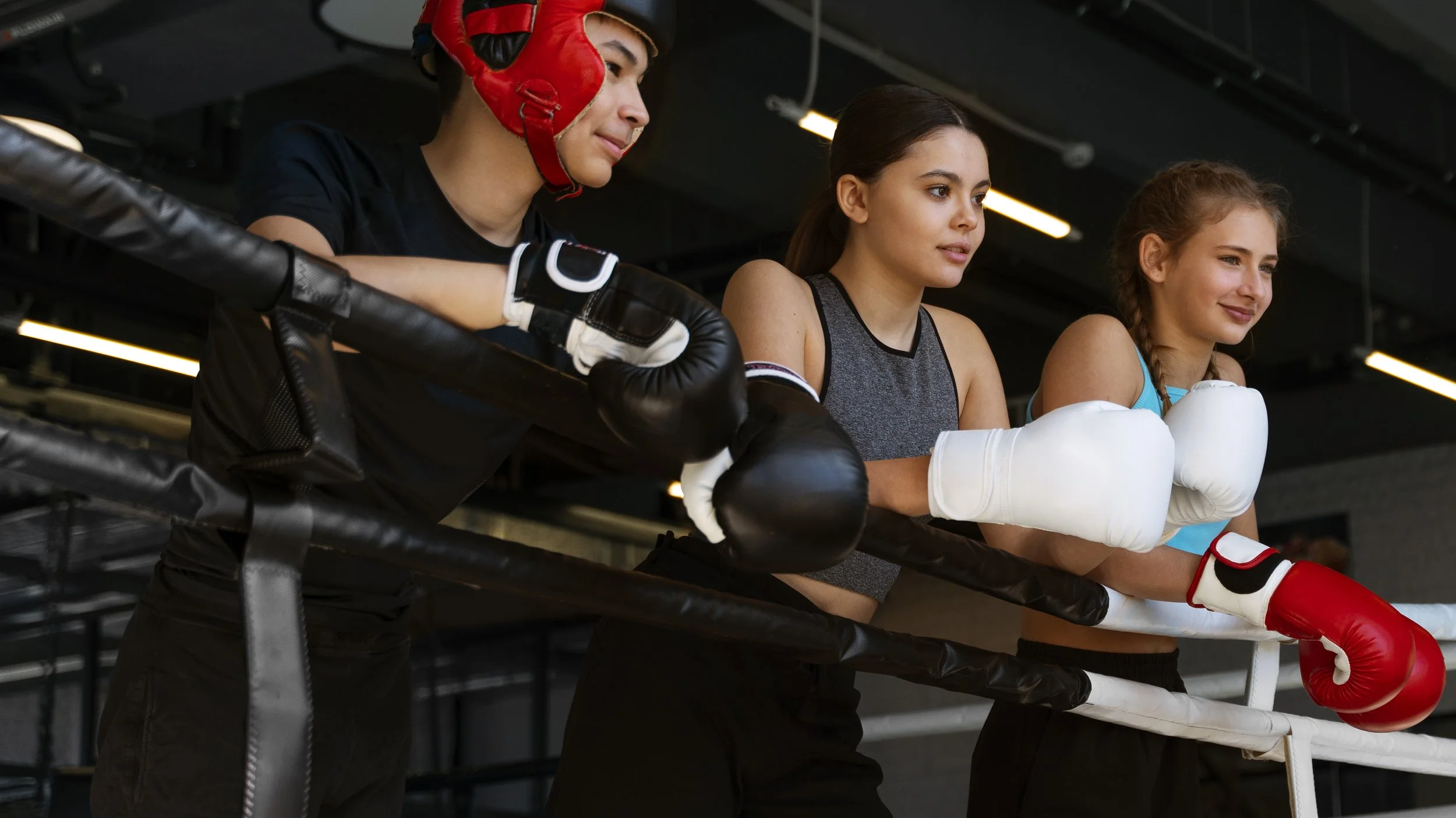 Drei junge Frauen in Boxhandschuhen im Boxring, die zuschauen.
