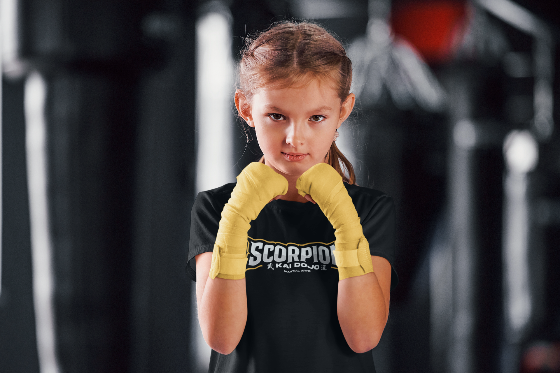 Kampfsportlerin in einer Kampfhaltung im Fitnessstudio, mit gelben Boxhandschuhen, schwarze T-Shirt mit dem Schriftzug 'Scorpion Kai Doyo Martial Arts'.