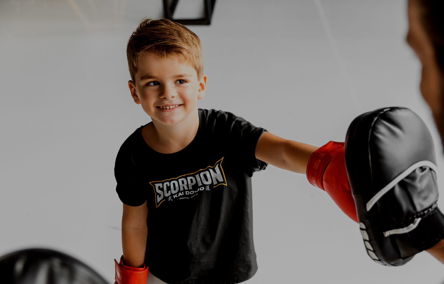 Ein kleiner Junge trägt Boxhandschuhe und macht einen Schlag gegen einen Partner, der ebenfalls Boxhandschuhe trägt, in einem Boxtraining.