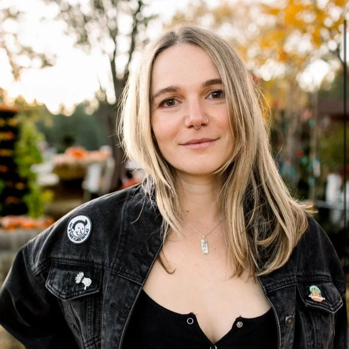 A woman wearing a black crop top and black jean jacket smiles softly at the camera.