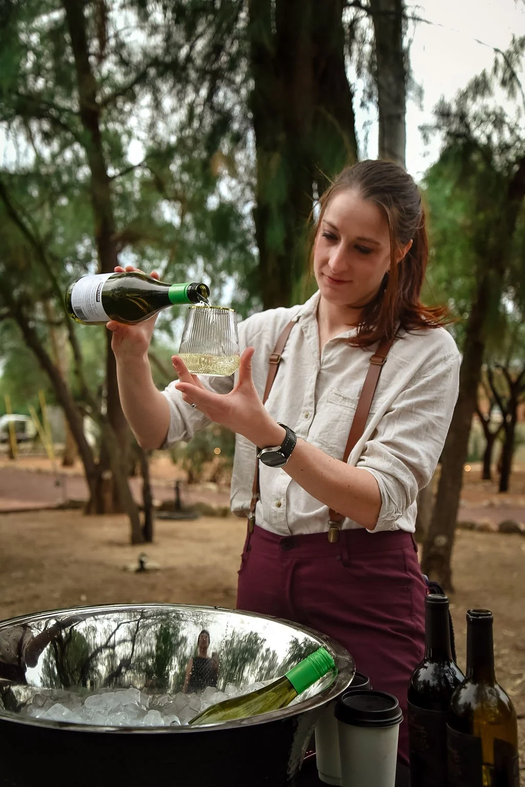 A bartender pours white wine into a glass at an outdoor wedding.