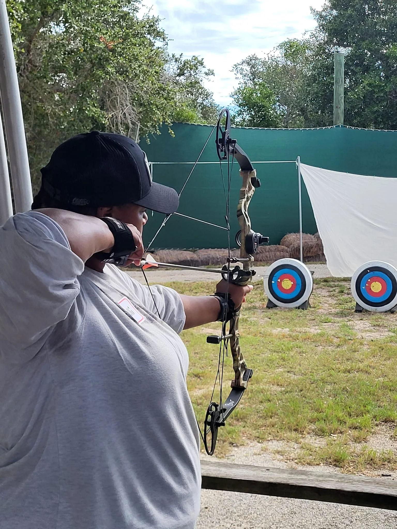 Person practicing archery outdoors, aiming a compound bow at archery targets.