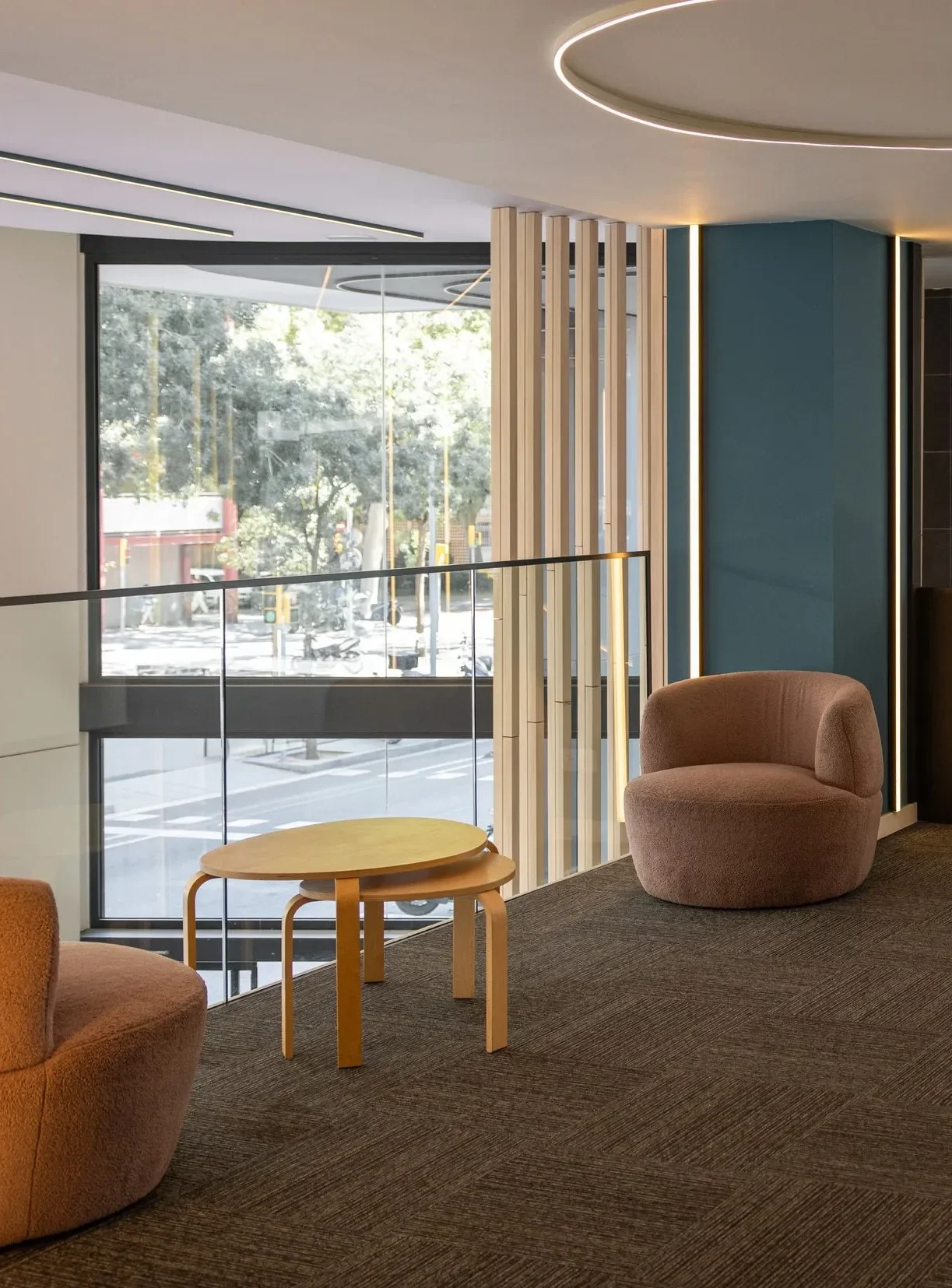 Interior moderno con sillones y mesa de madera en un espacio con ventanas grandes y vista a la calle.