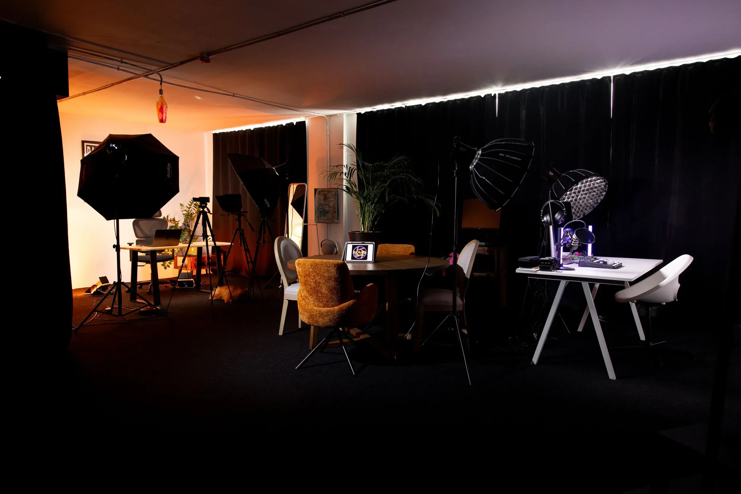 Estudio de fotografía o videografía con equipo de iluminación y fondo oscuro, mesas y sillas para producción.