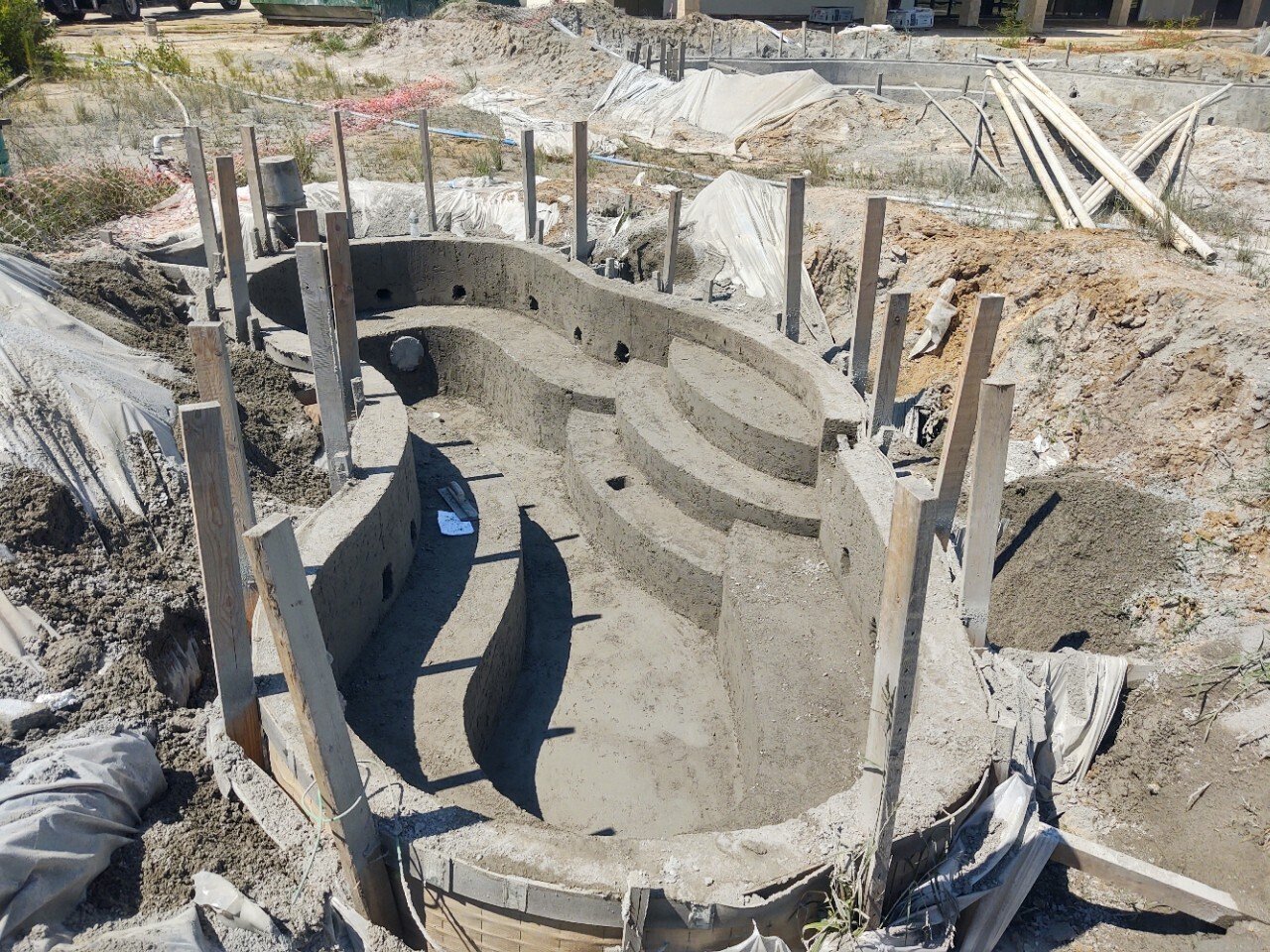 Concrete swimming pool under construction with rounded steps, surrounded by building supports and construction materials.