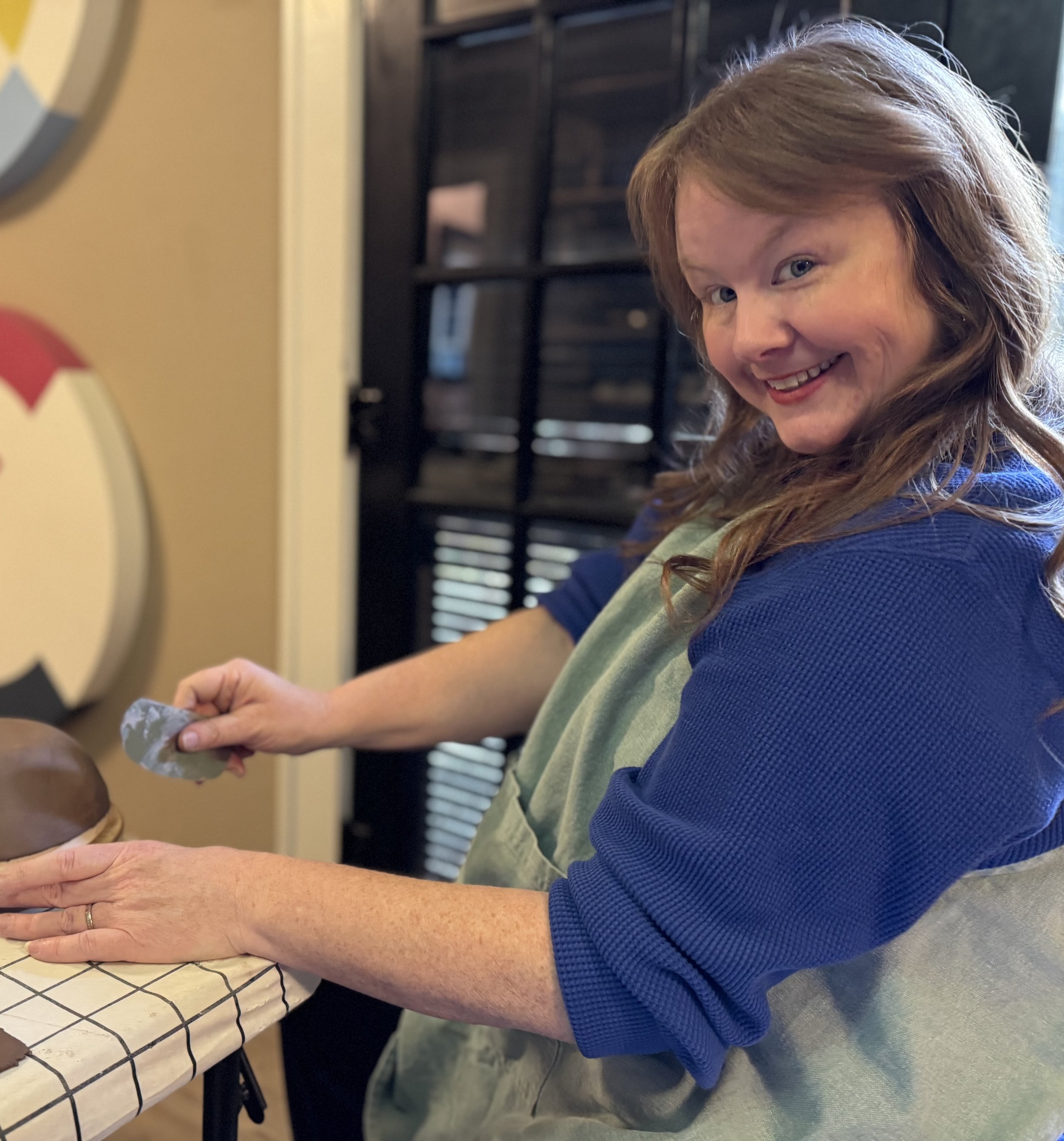 Person in blue shirt and apron sculpting clay