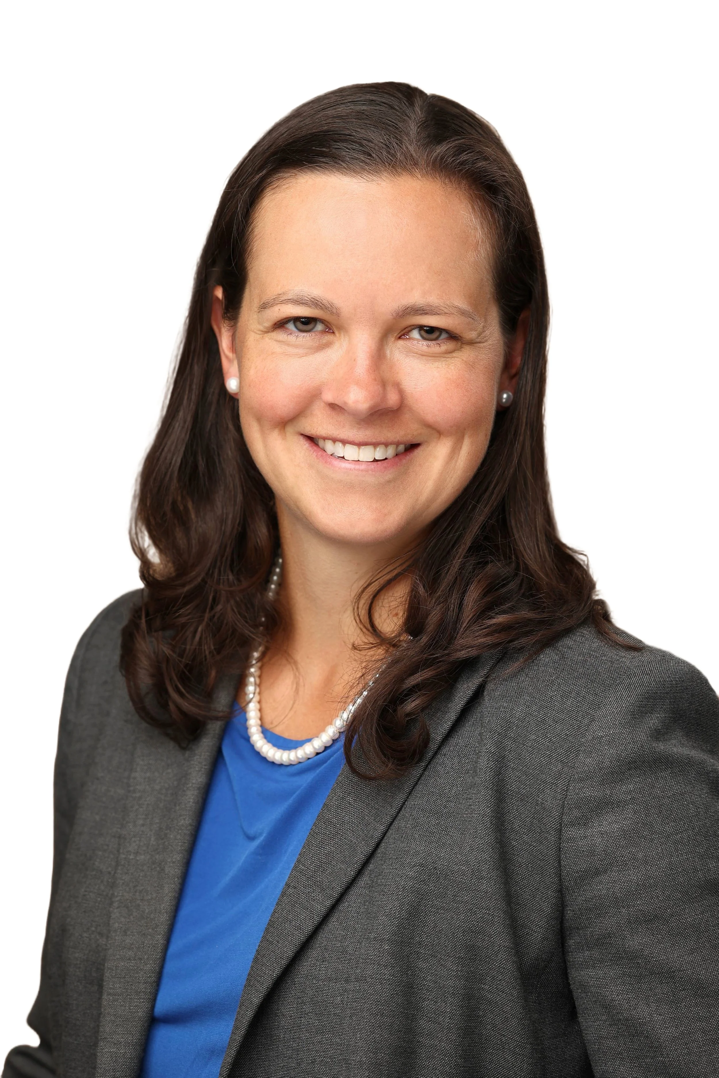 A professional woman with dark brown hair in a shoulder-length style, wearing a gray blazer, a blue blouse, a pearl necklace, and pearl earrings, smiling against a white background.