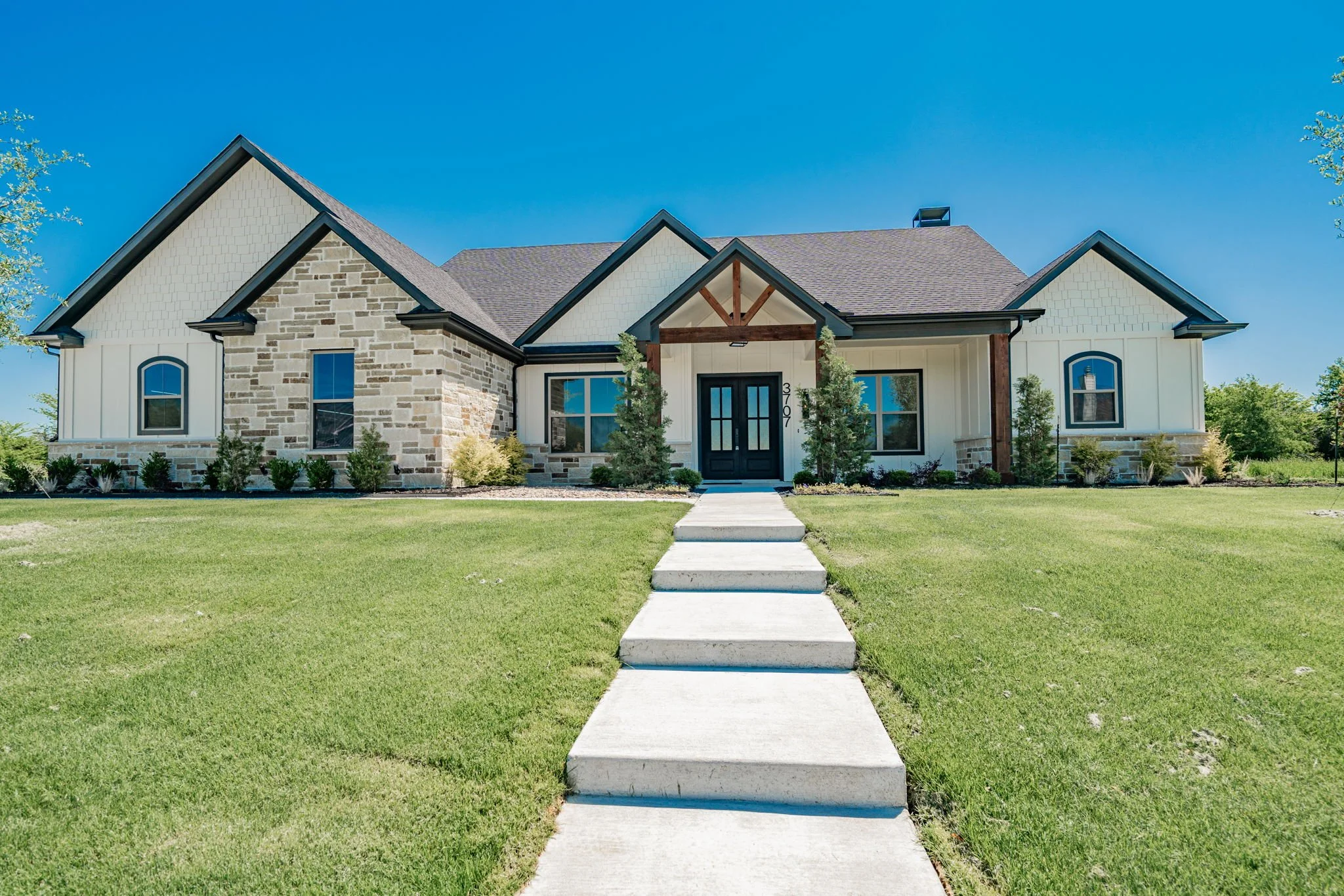 Modern single-story house with stone and siding exterior, gabled roof, front porch, and green lawn.