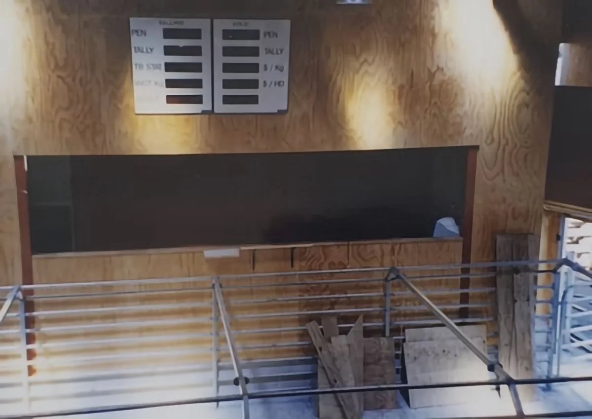 Interior of a building with a wooden wall, a blackboard, a white menu board, and a metal railing in the foreground.