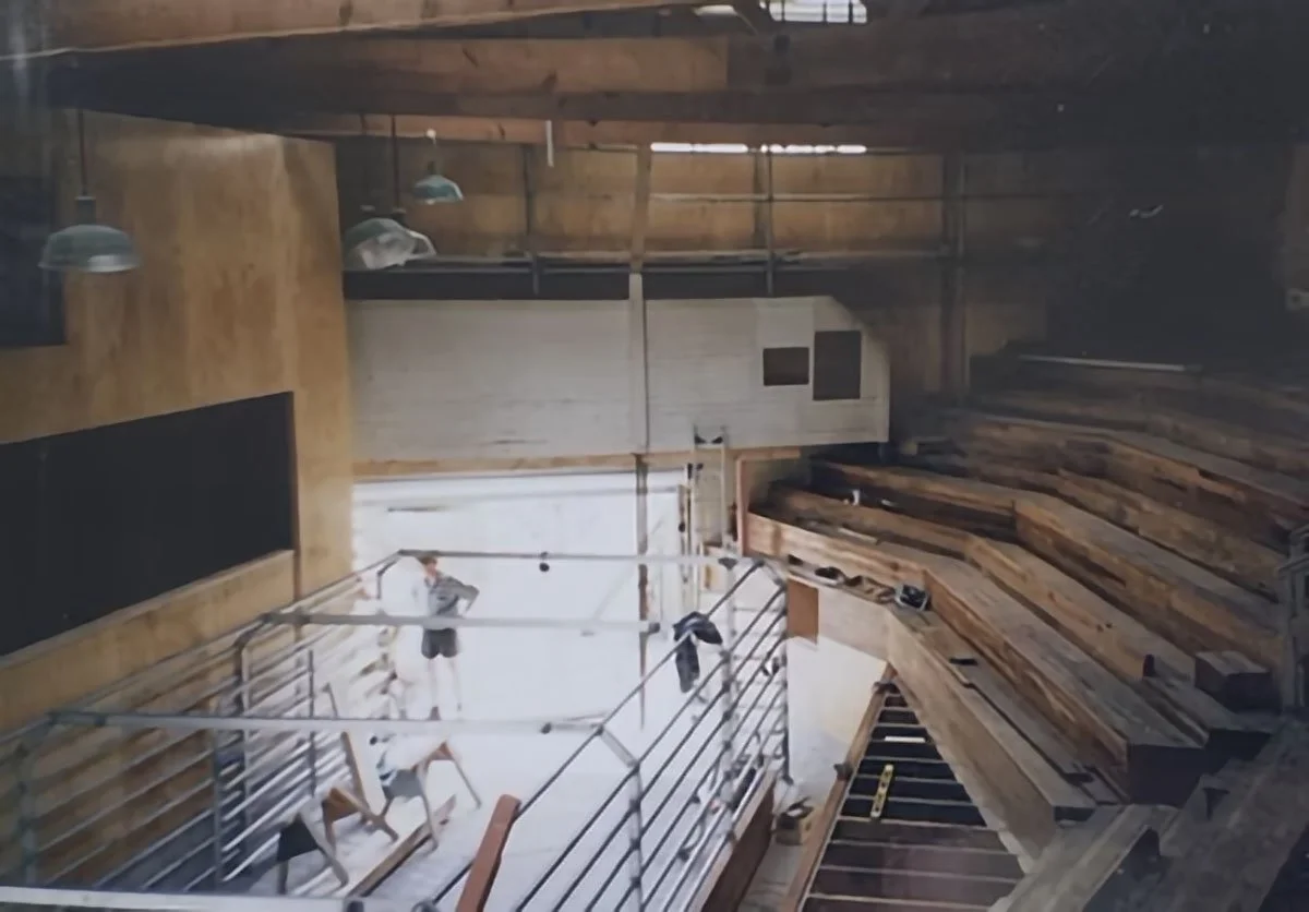 Interior of a wooden auditorium or theater under construction with seating and scaffolding.