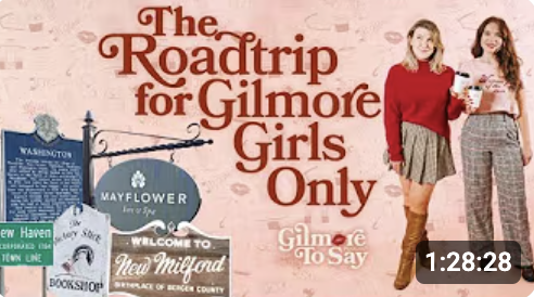 Signboard with text "The Roadtrip for Gilmore Girls Only" and two young women standing in front, smiling and holding drinks.