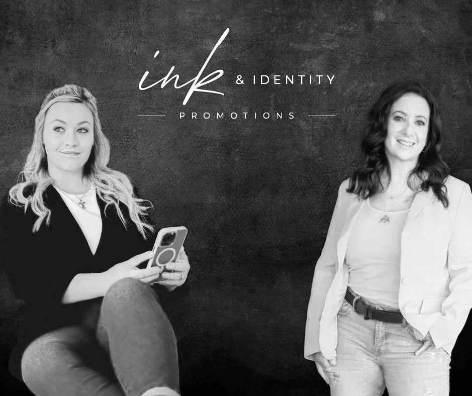 Two women standing against a wall with the text 'ink & IDENTITY PROMOTIONS' written in a stylish font.