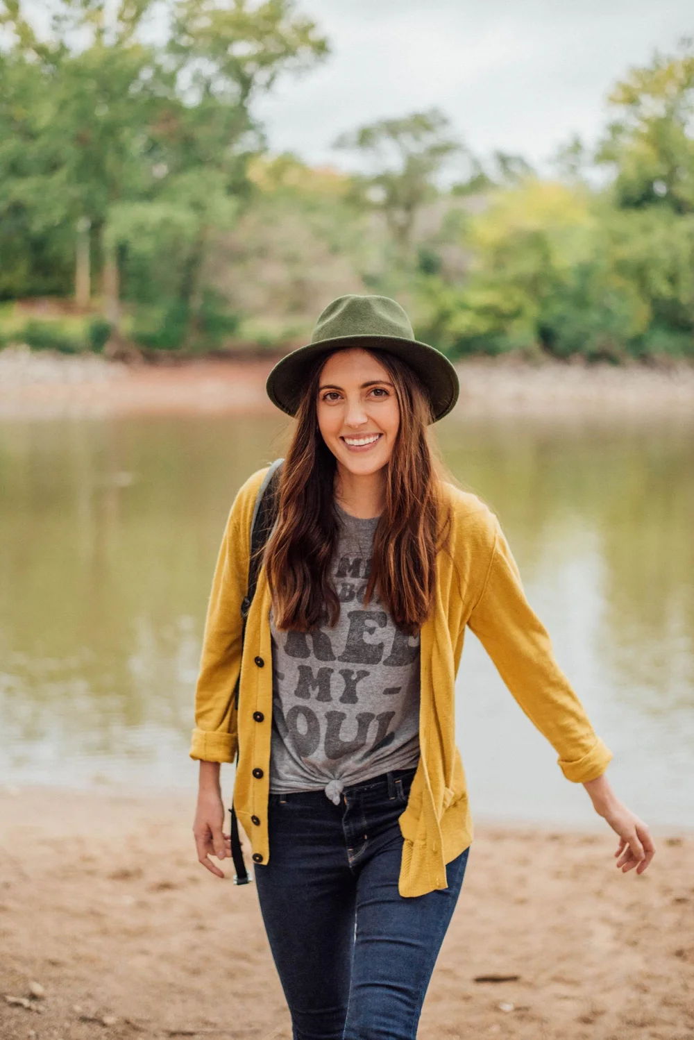 Morgan smiling beside the water in a green hat and yellow cardigan