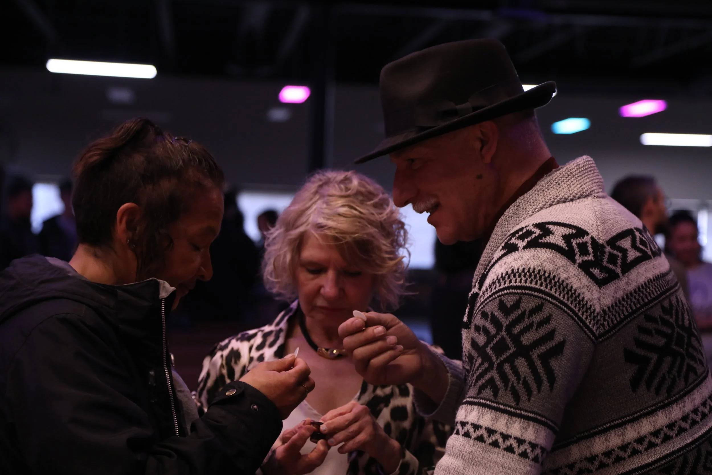 Three people examining an object in a dimly lit indoor setting.