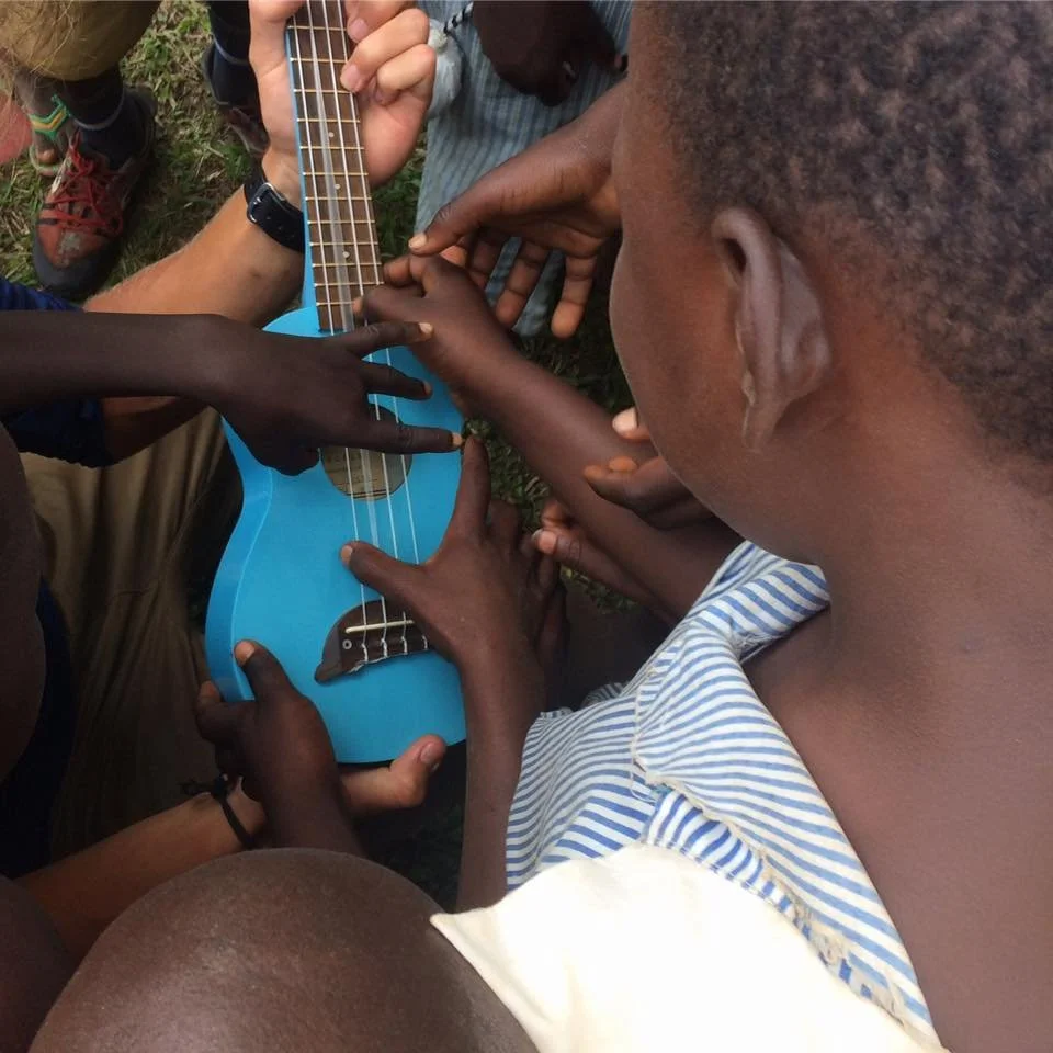 High angle shot of children from Uganda holding and touching a bright blue ukelele