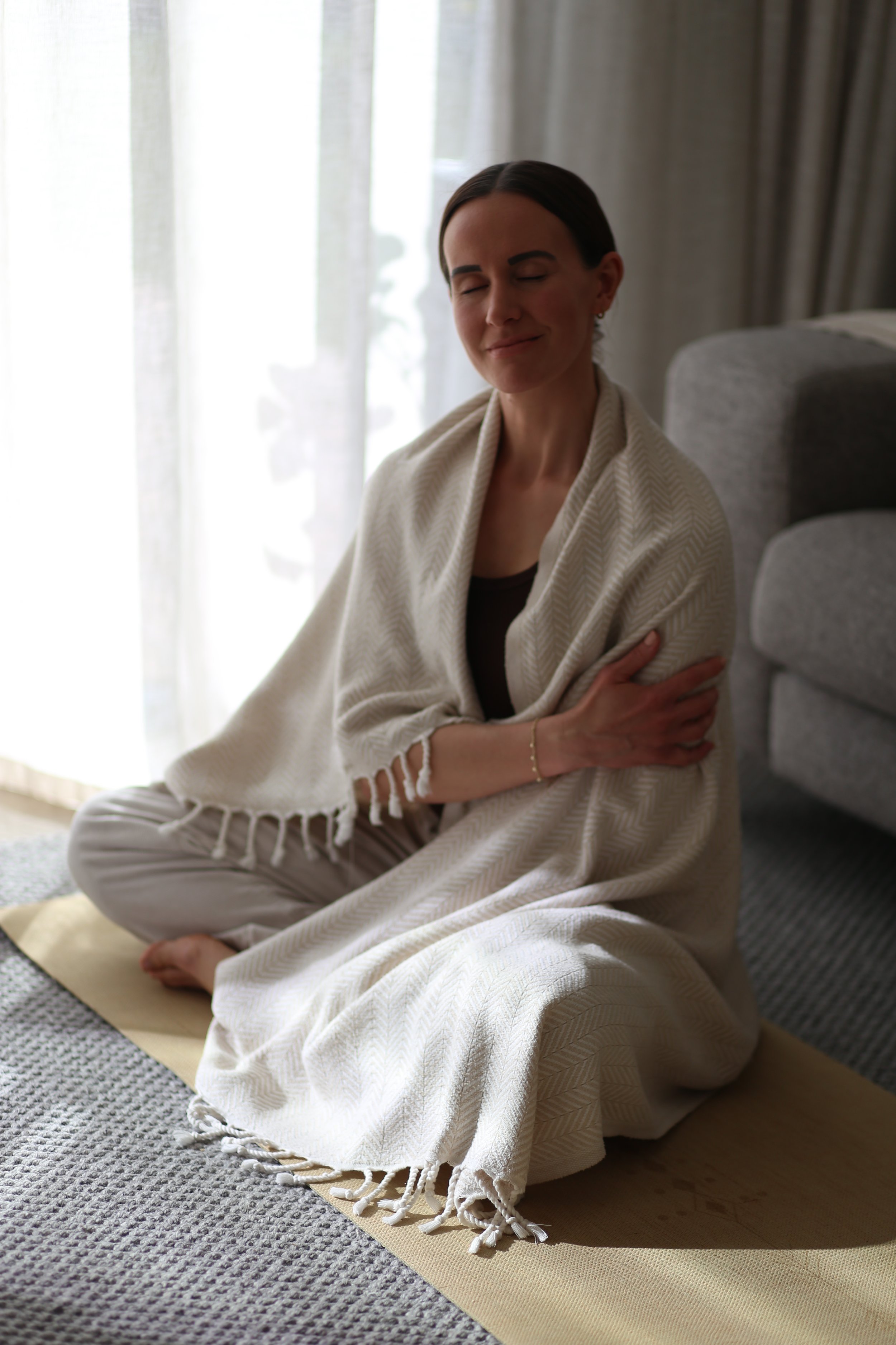 Holistic wellness coach - Alex Ballagh - is taking a mindful moment on the floor, sitting cross-legged with her eyes closed.