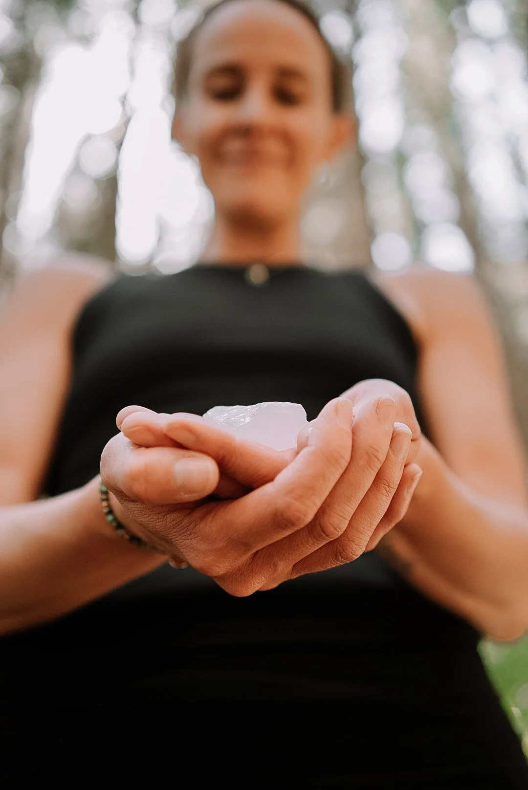 Low angle shot of holistic wellness coach - Alex Ballagh - holding a Rose Quartz crystal in the palm of her hands.