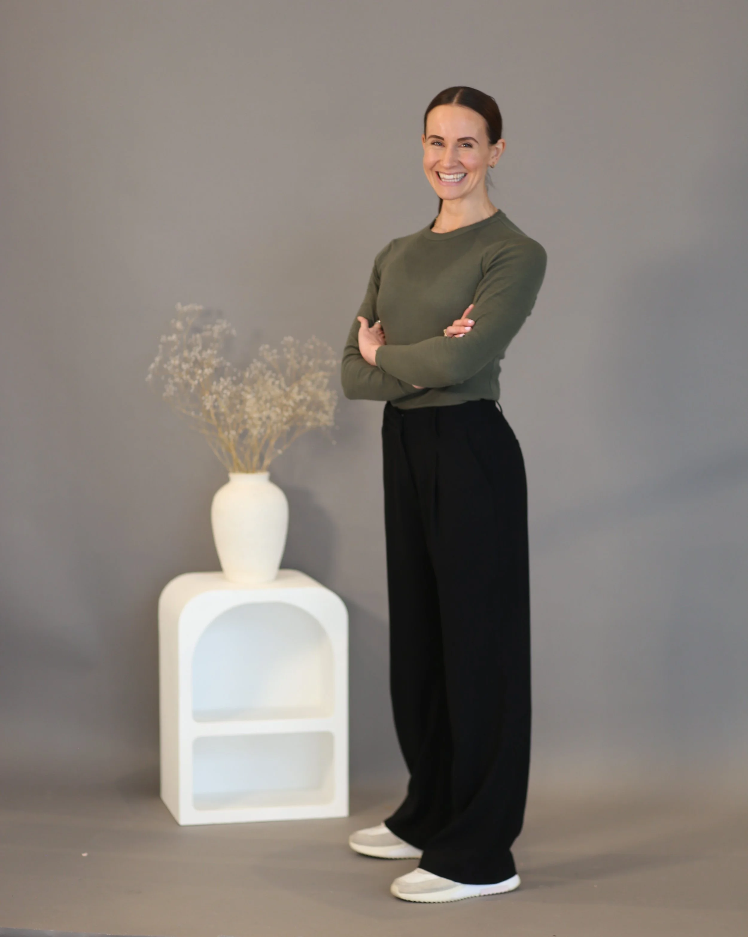 Holistic wellness coach - Alex Ballagh - is standing side on and smiling towards the camera.
