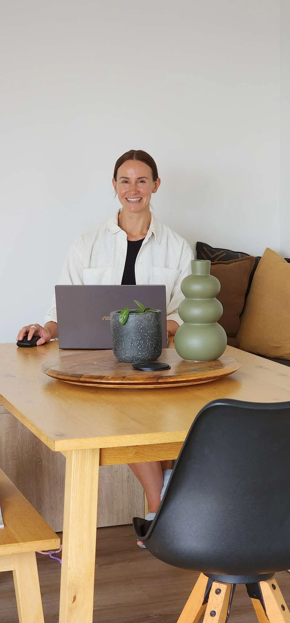 Holistic wellness coach - Alex Ballagh - is sitting at a table with her laptop and smiling at the camera.