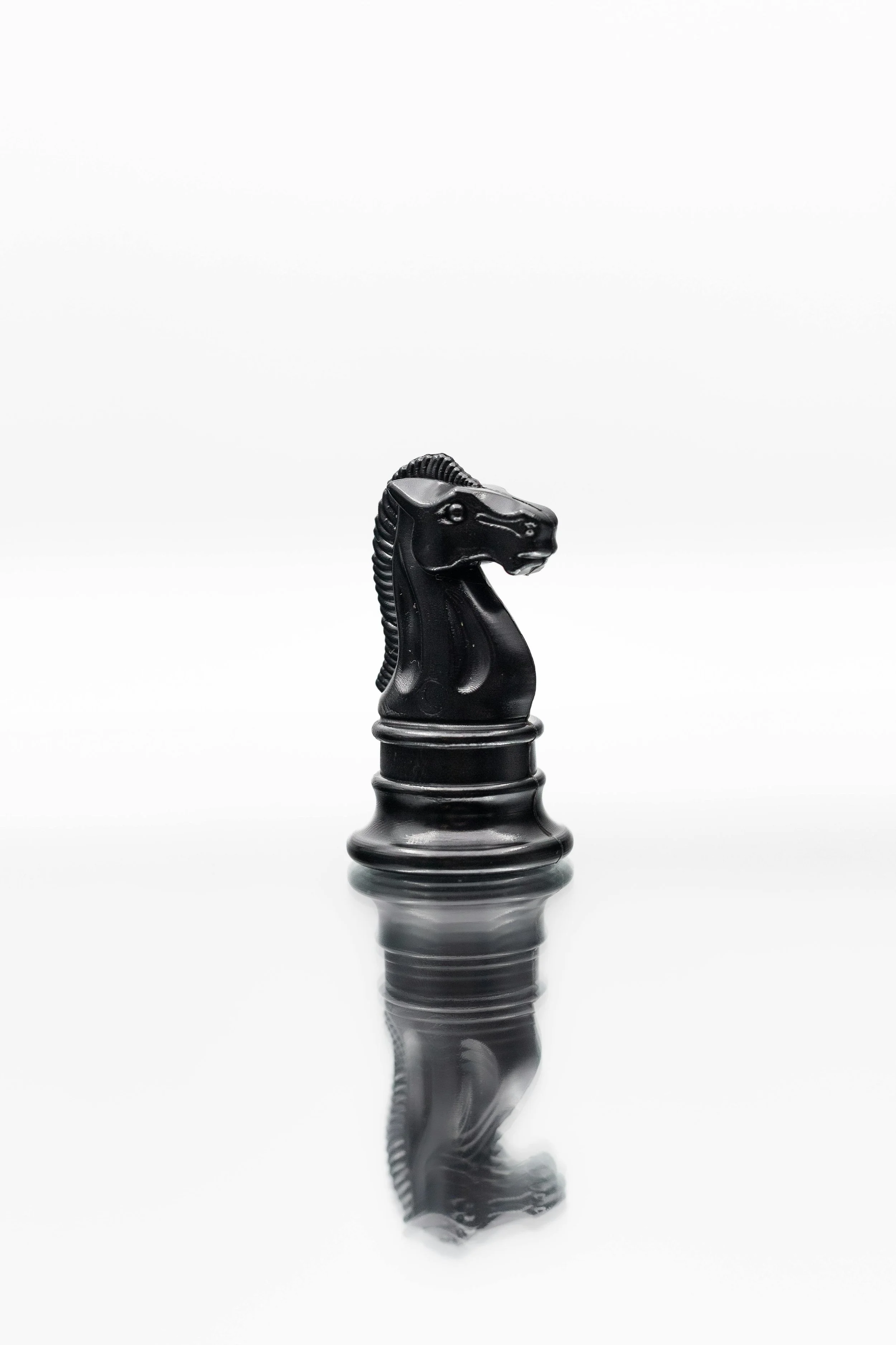 A black king chess piece on a reflective surface with a blurred white background.