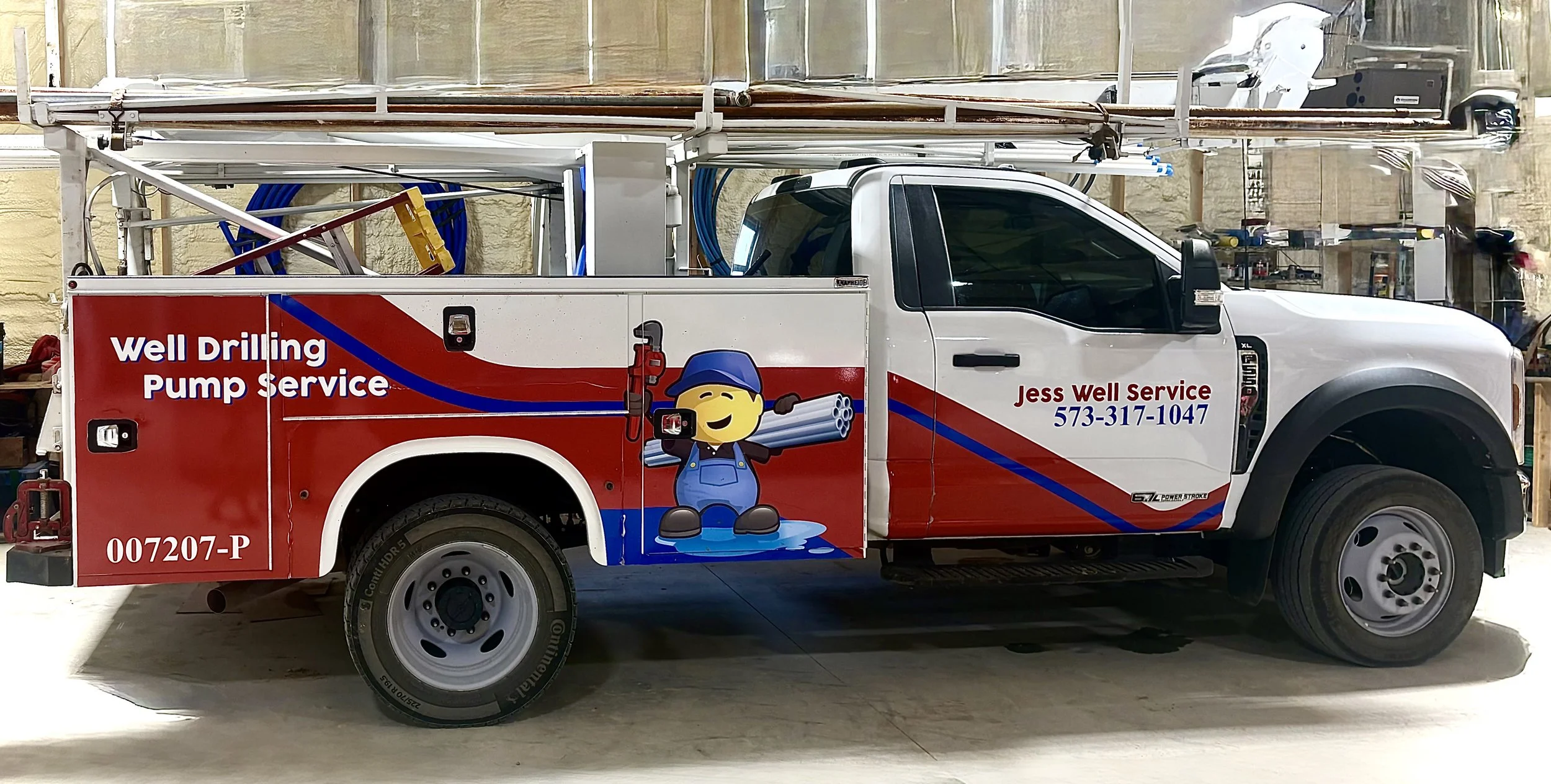 A white service truck with red and blue graphics, advertising Jess Well Service. The truck features a cartoon character of a smiling welder holding pipes and a welding torch. The text on the truck includes 'Well Drilling Pump Service,' the company's phone number, and logo.