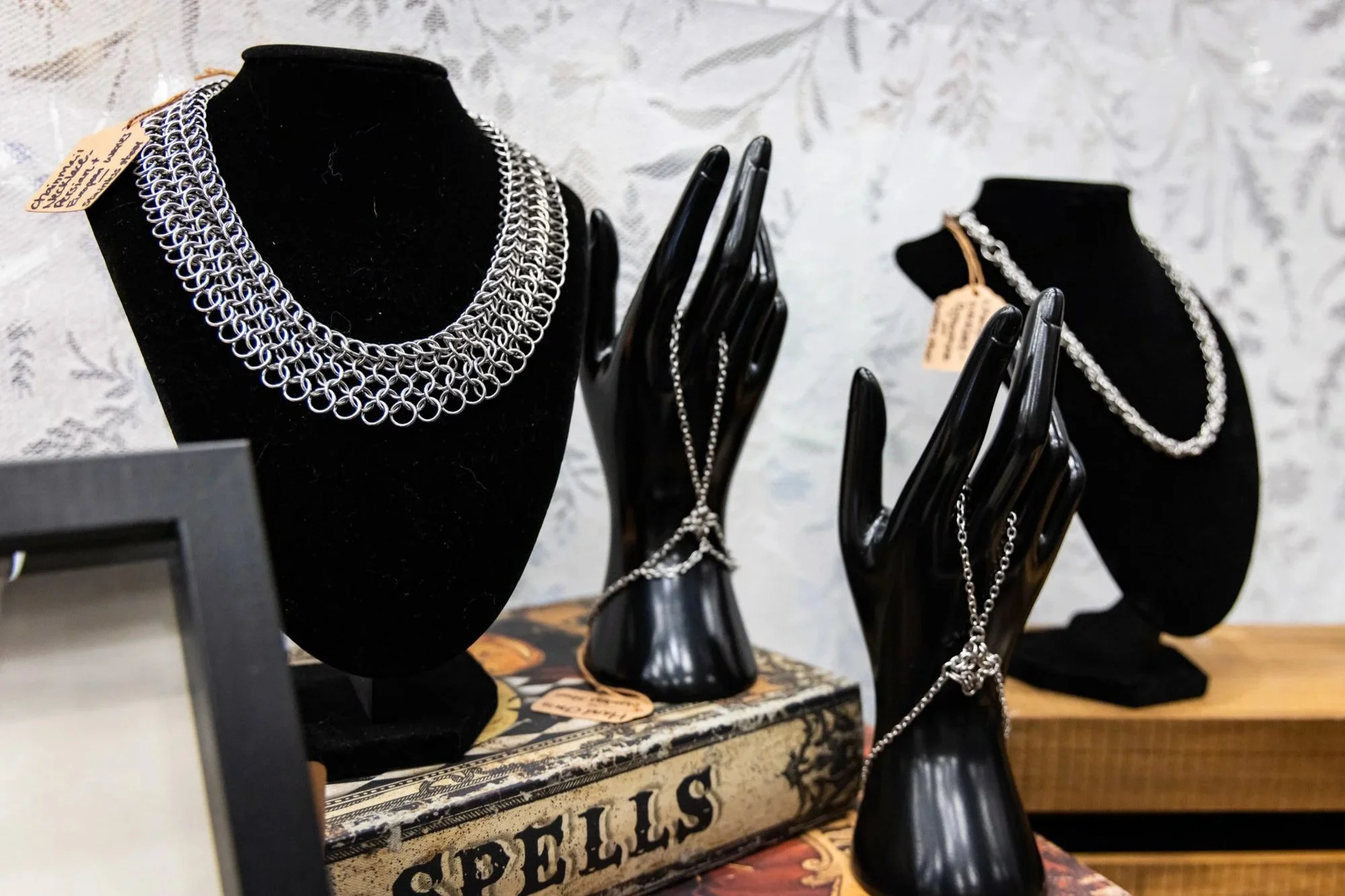 Display of chainmail jewelry, including necklaces and earrings, on black busts and hands in a jewelry shop.