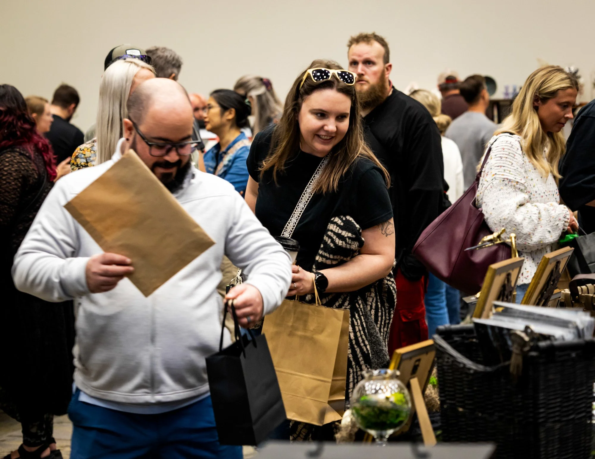 People browsing at an indoor craft fair or market, looking at handmade items and displays, with a diverse crowd and a casual atmosphere.