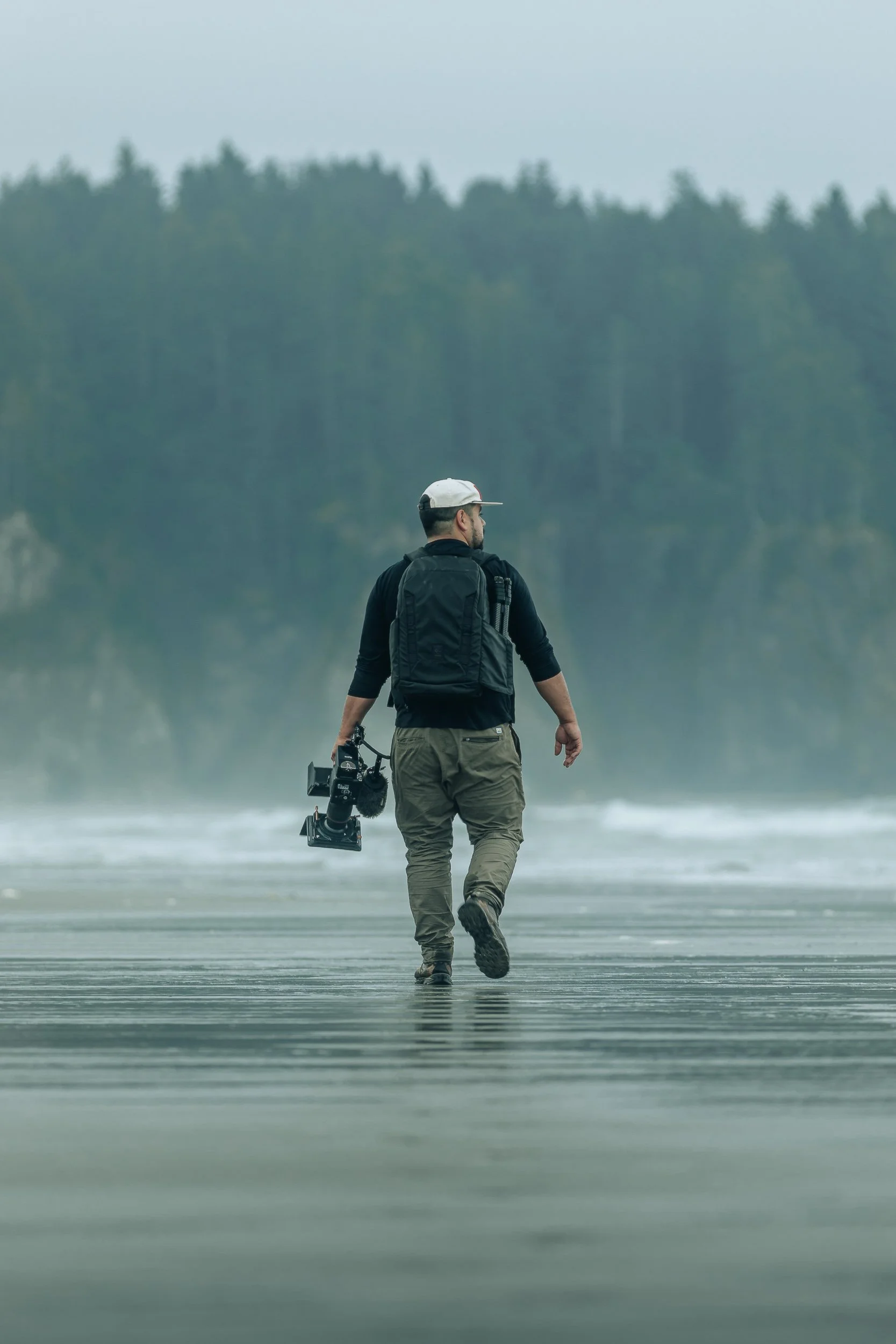 Photographer walking with camera gear on a foggy beach on the Olympic Peninsula, behind the scenes outdoor photography by James Brasier