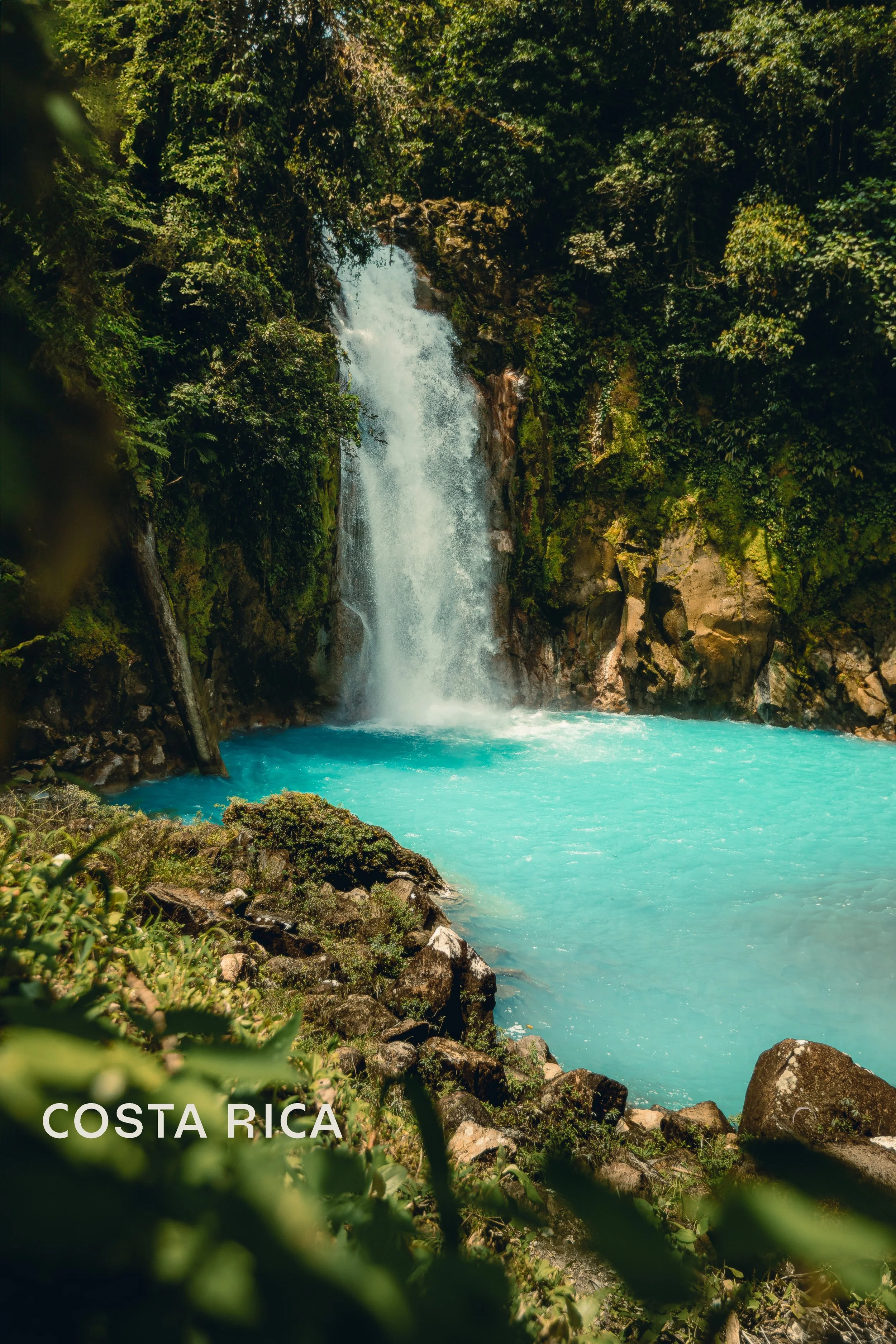 Rio Celeste waterfall flowing into turquoise blue pool surrounded by tropical rainforest, Costa Rica adventure travel photography by James Brasier