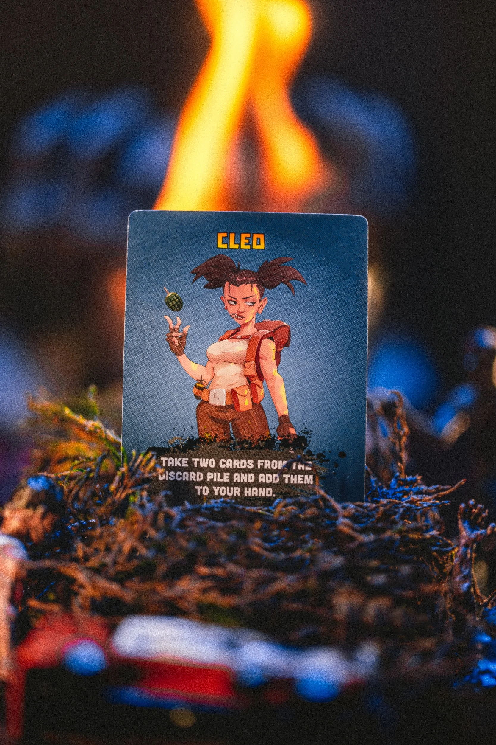 ZETA Survival Cleo character card with fire and blue lighting on moss, product photography by James Brasier